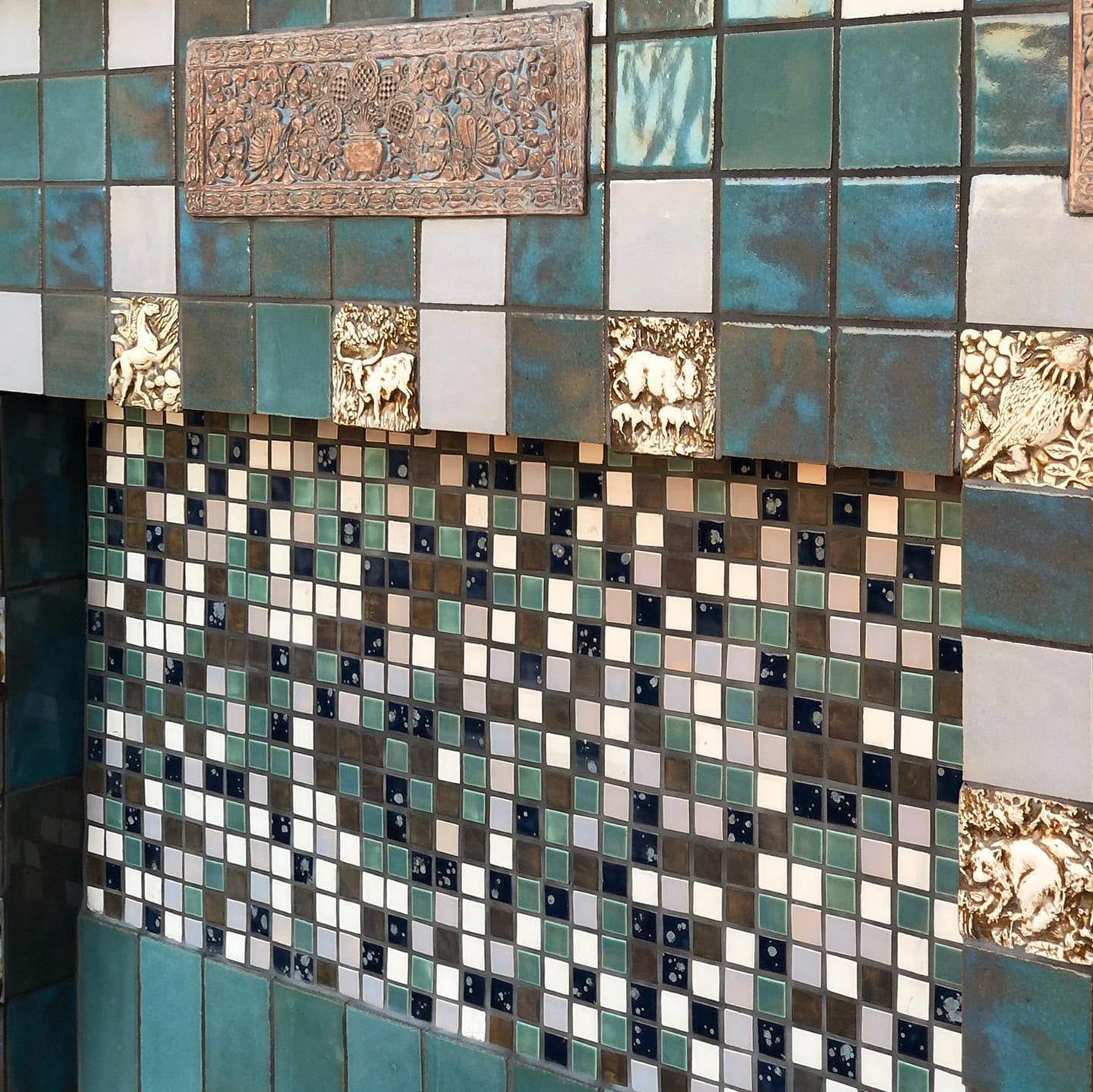 Wall with mosaic and square tiles in shades of blue, green, and brown, with decorative relief panels.