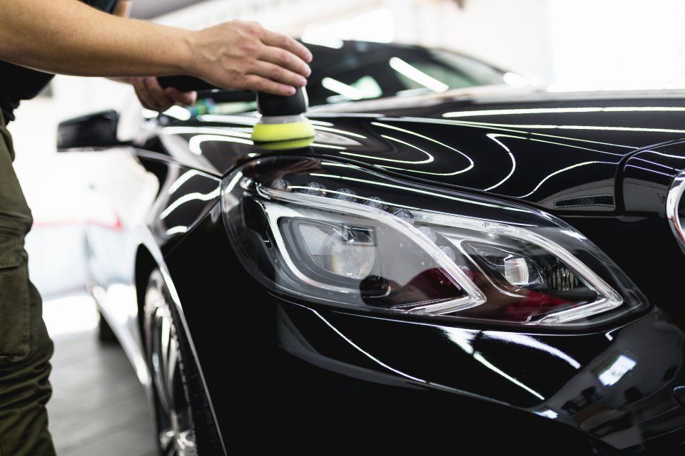 A man is polishing the hood of a black car.