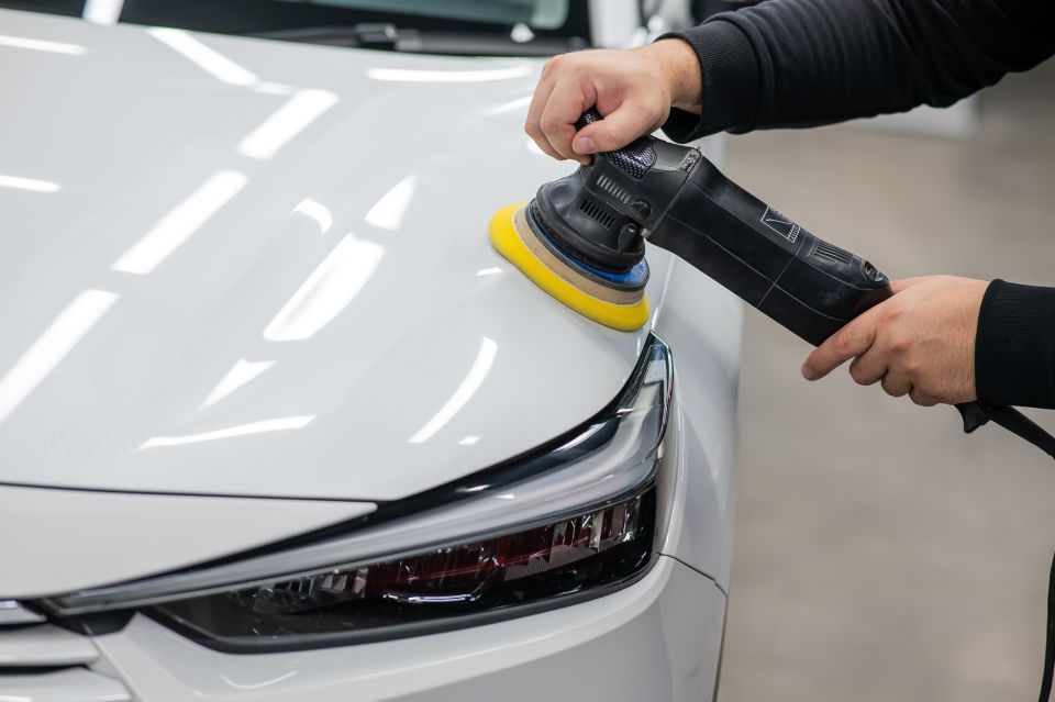 A person is polishing a white car with a machine.