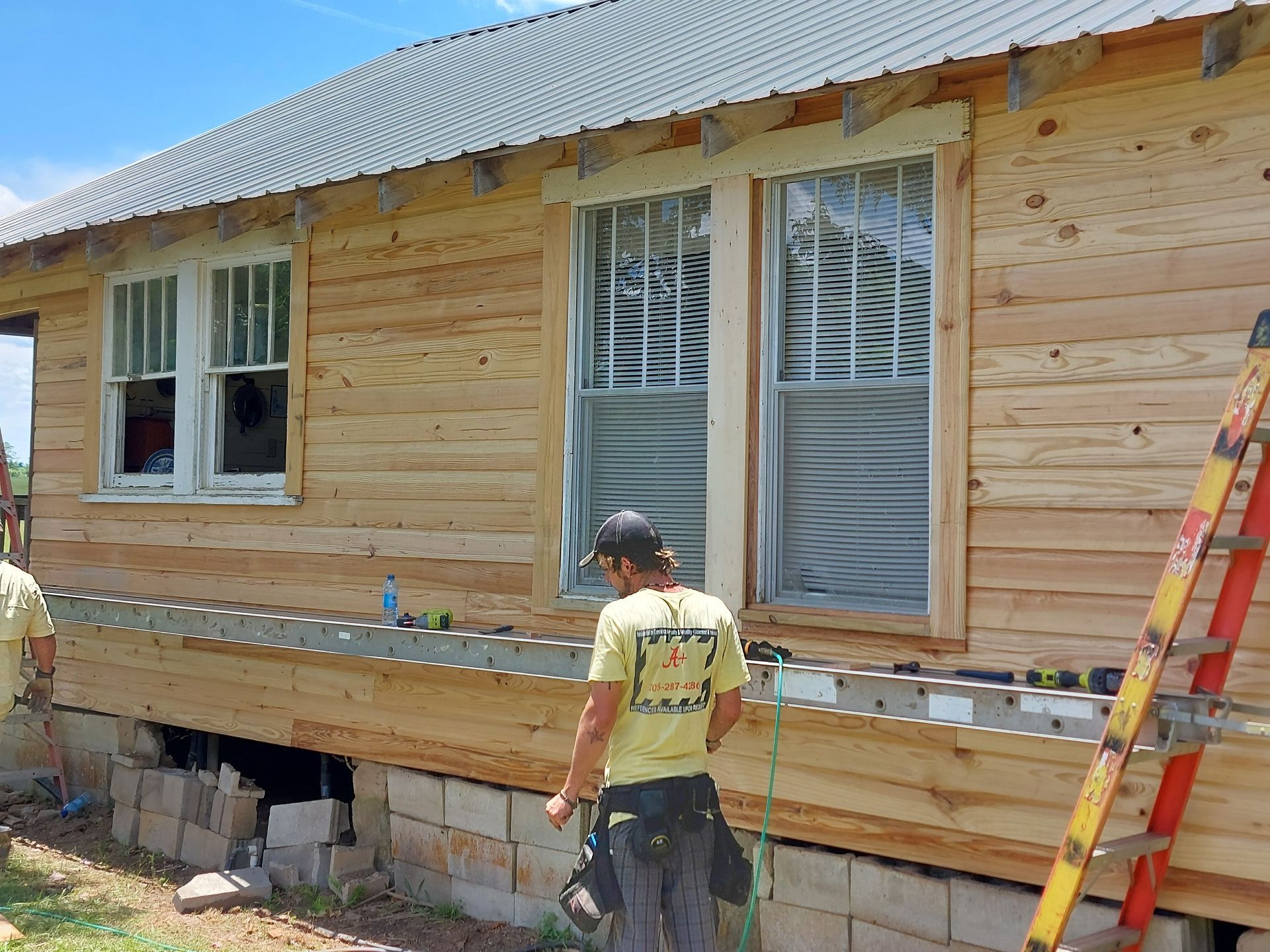 Person working on exterior house siding with ladder and window during construction