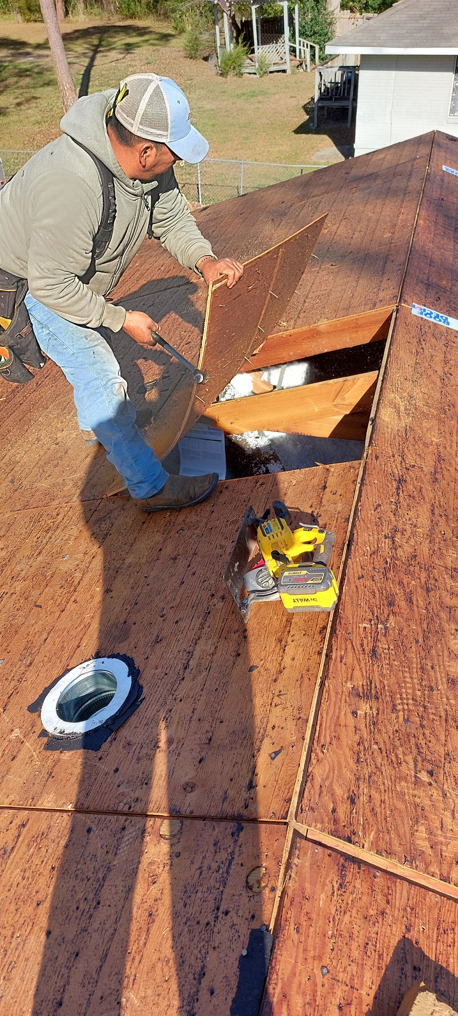 Worker on a sloped roof installing shingles near a roof vent and blue bucket