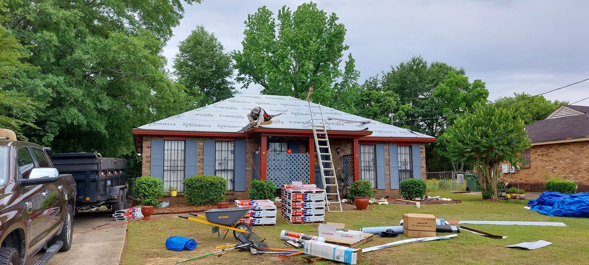 Front yard with a brick house, ladders, scattered tools, and landscaping materials