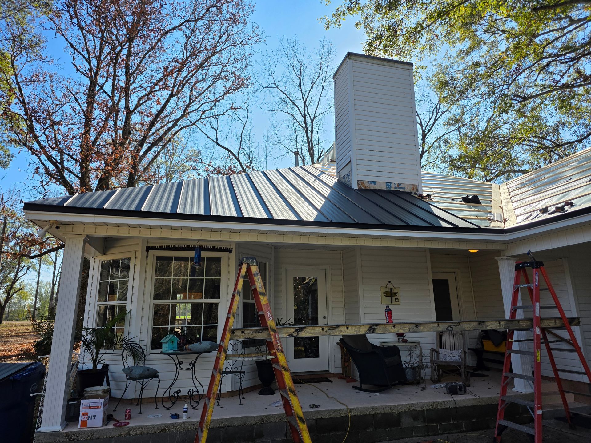 House exterior with a metal roof, chimney, and two ladders on the front porch during repair work