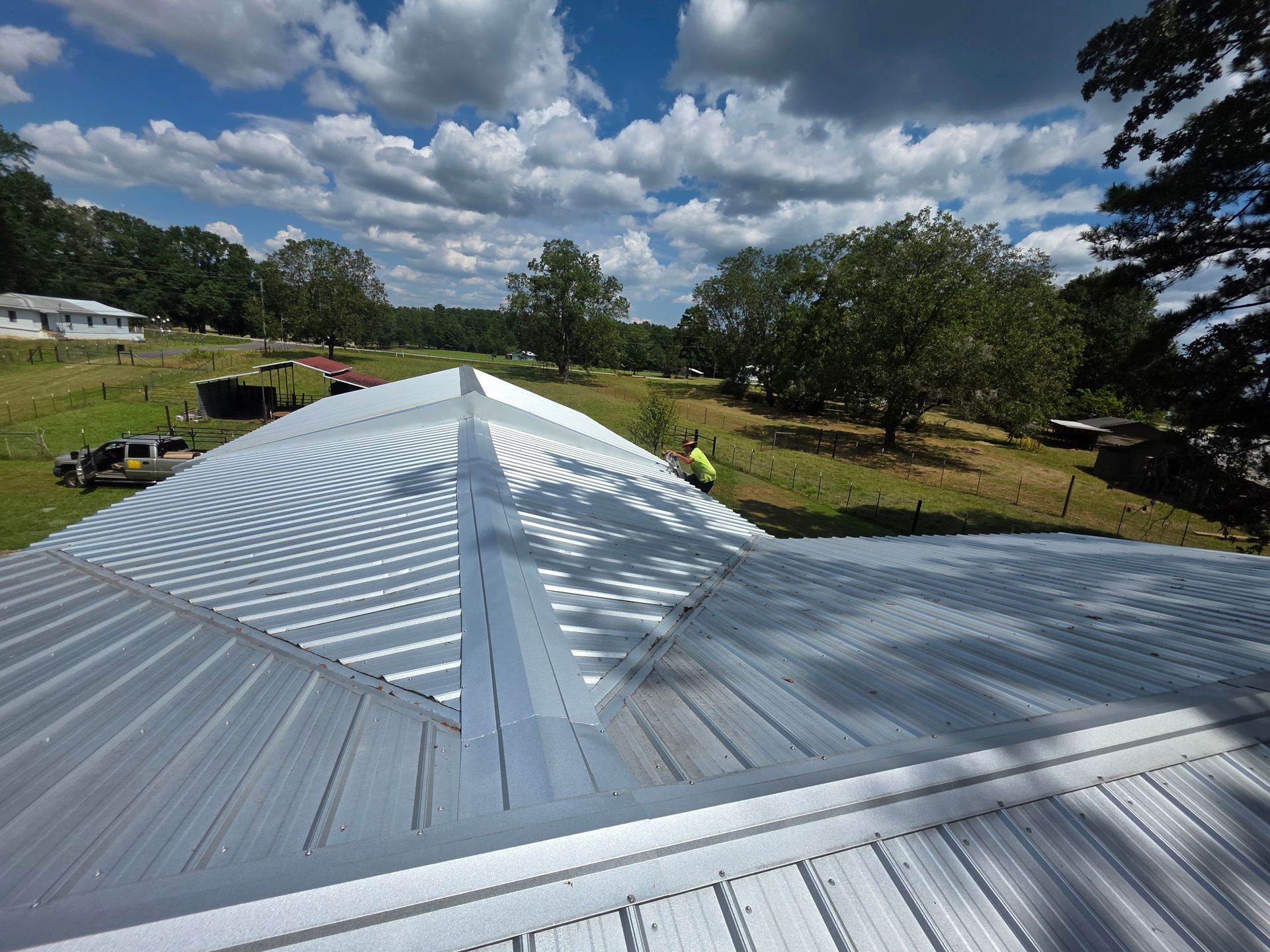 White metal roof under a cloudy sky, overlooking grassy fields and trees