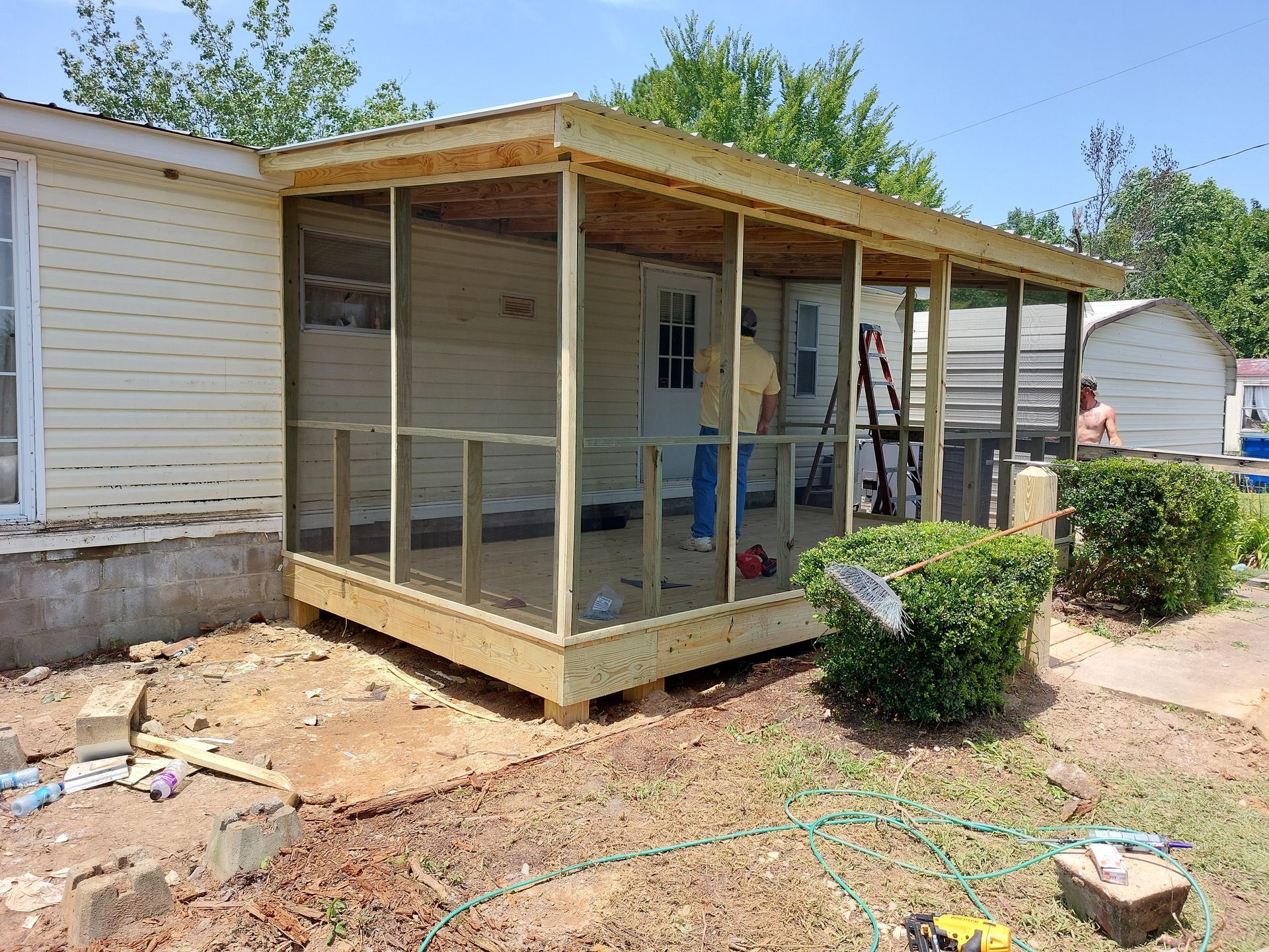 Screened porch addition on a house with unfinished wooden framing and beige siding.
