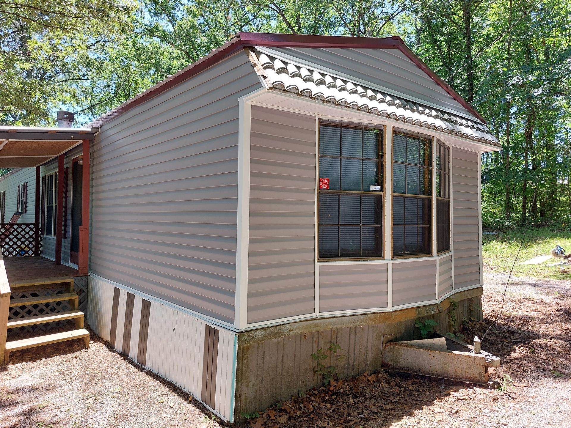 Small beige mobile home with red roof and front windows, beside a wooded area