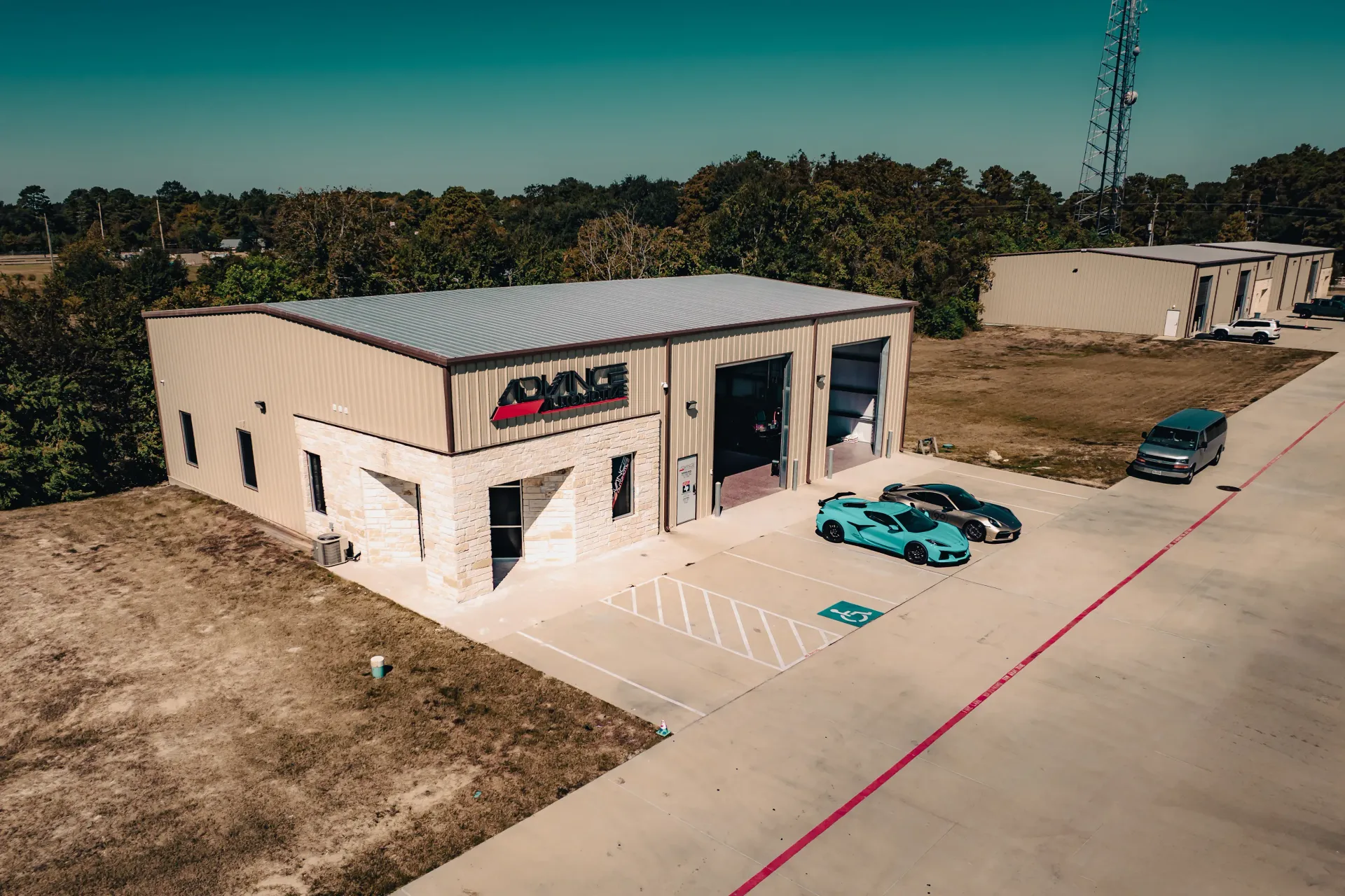 A tan building with two large garage doors, two sports cars outside, and a small building in the background. | Advance Automotive
