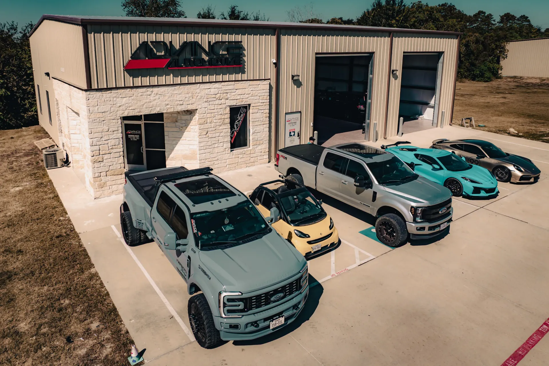 A garage with multiple vehicles parked outside. Gray truck in front, other vehicles include a Smart car and sports cars. | Advance Automotive