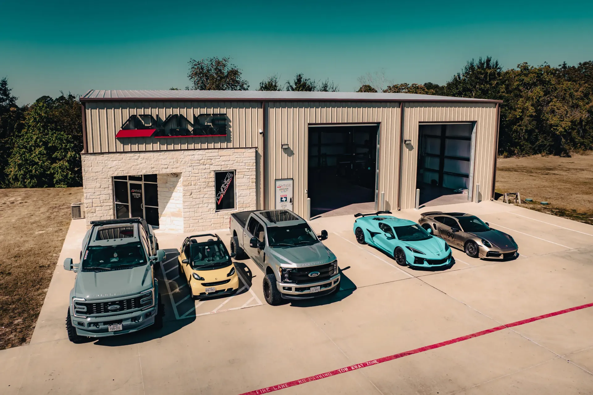 Cars parked outside a garage, including a truck, Corvette, and sedan, on a sunny day. | Advance Automotive