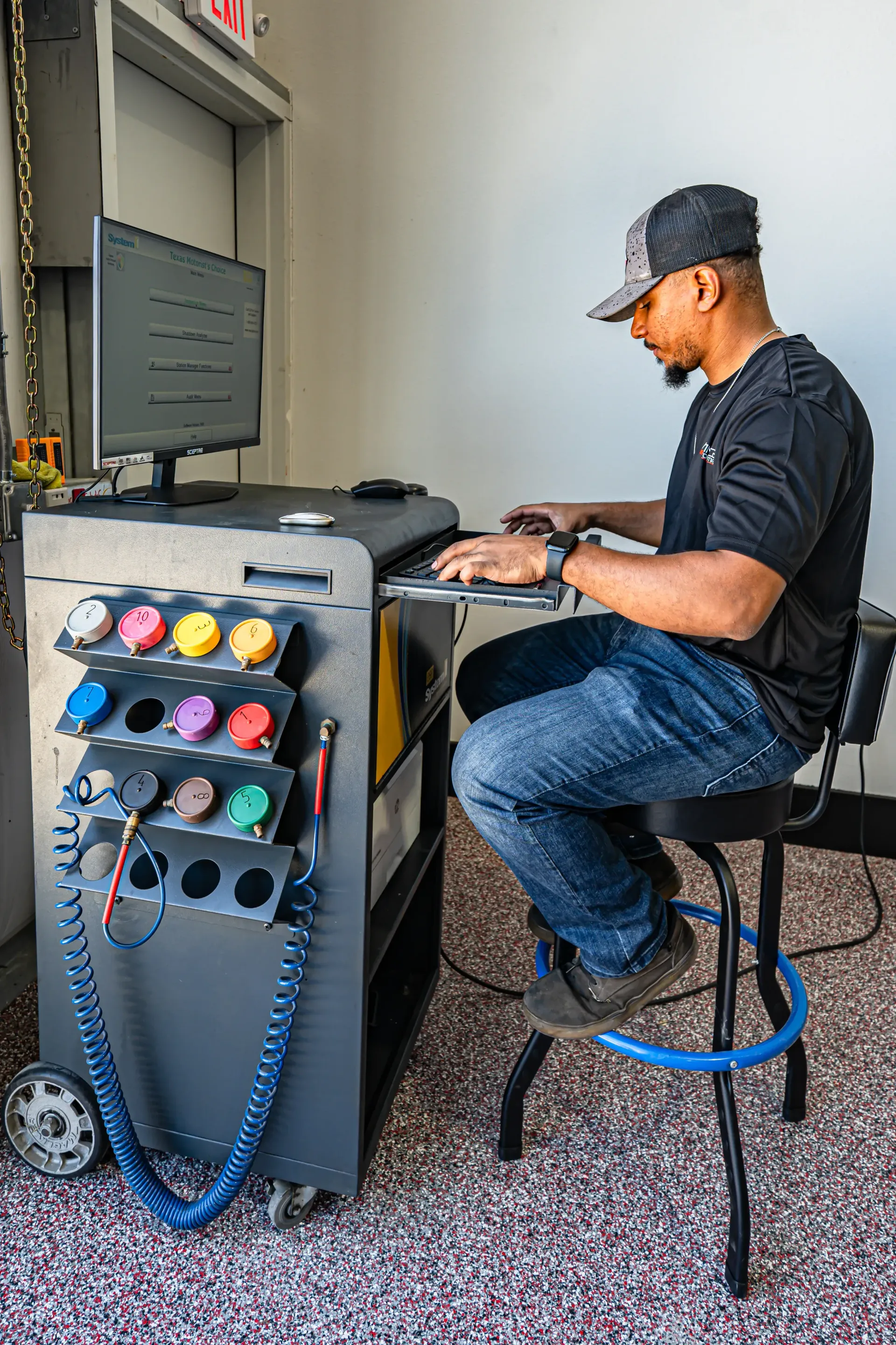 Man seated at a computer, working on a machine with colored connections, in a well-lit garage. | Advance Automotive
