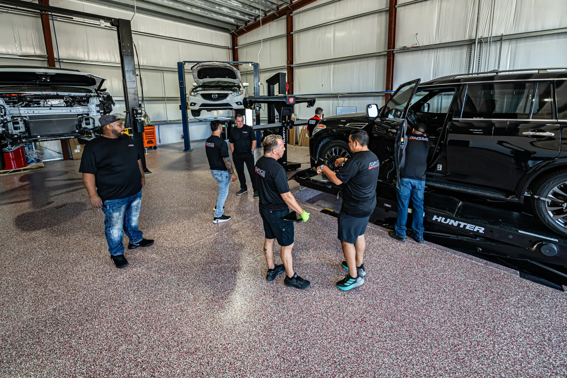 People working on a black SUV in a garage. Several people stand near the car, which is on a lift. | Advance Automotive