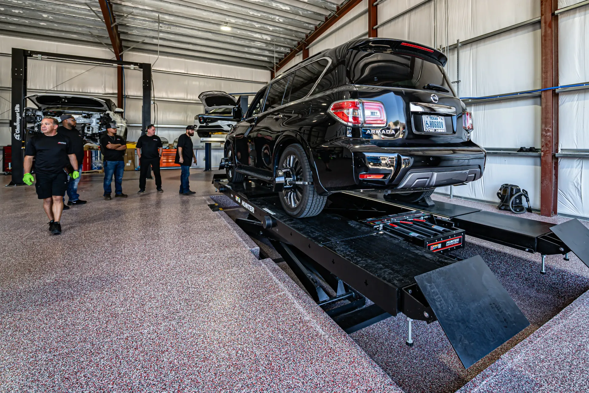 Black SUV on a lift in a garage, with mechanics observing. | Advance Automotive