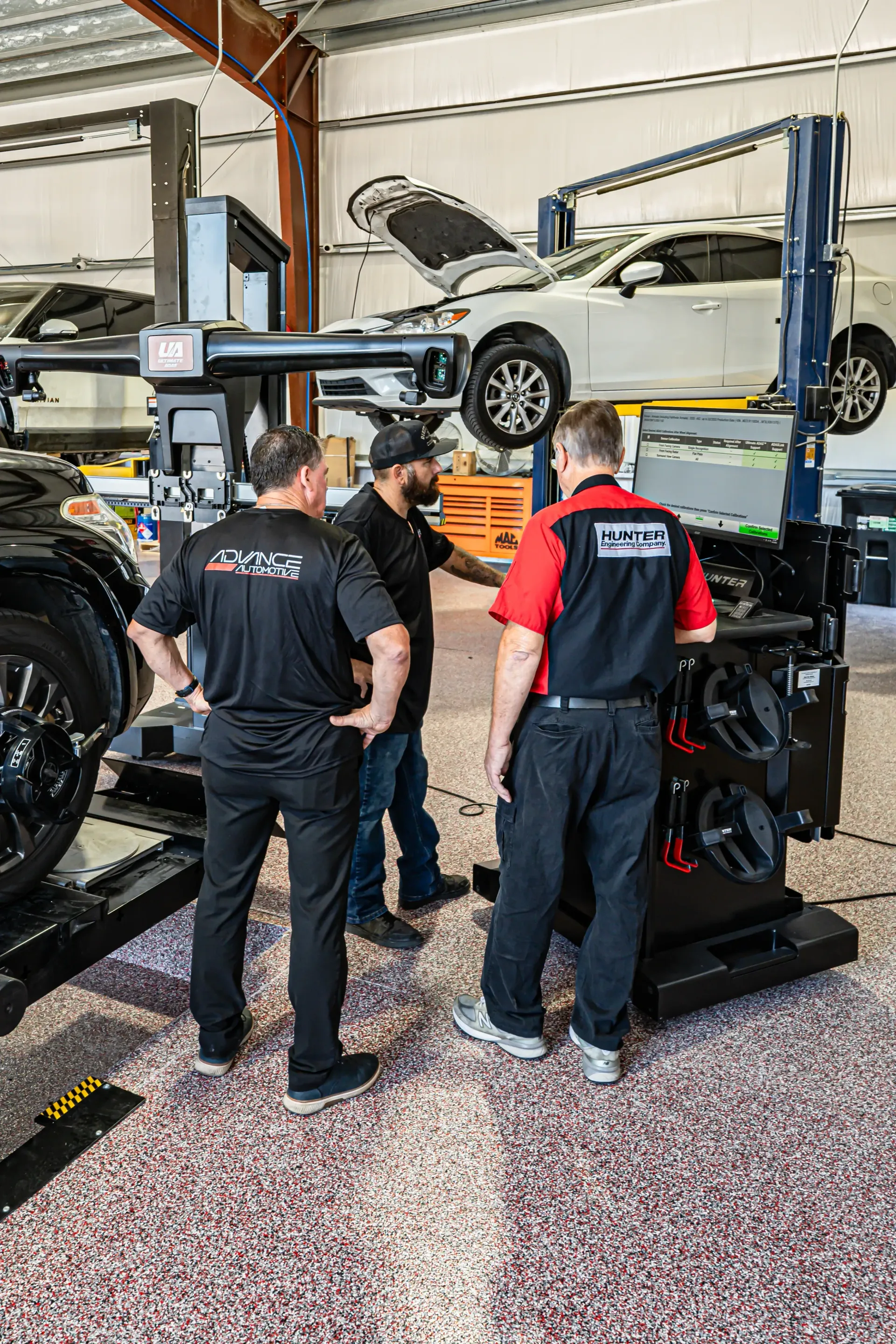 Three auto mechanics around a car alignment machine in a shop. | Advance Automotive