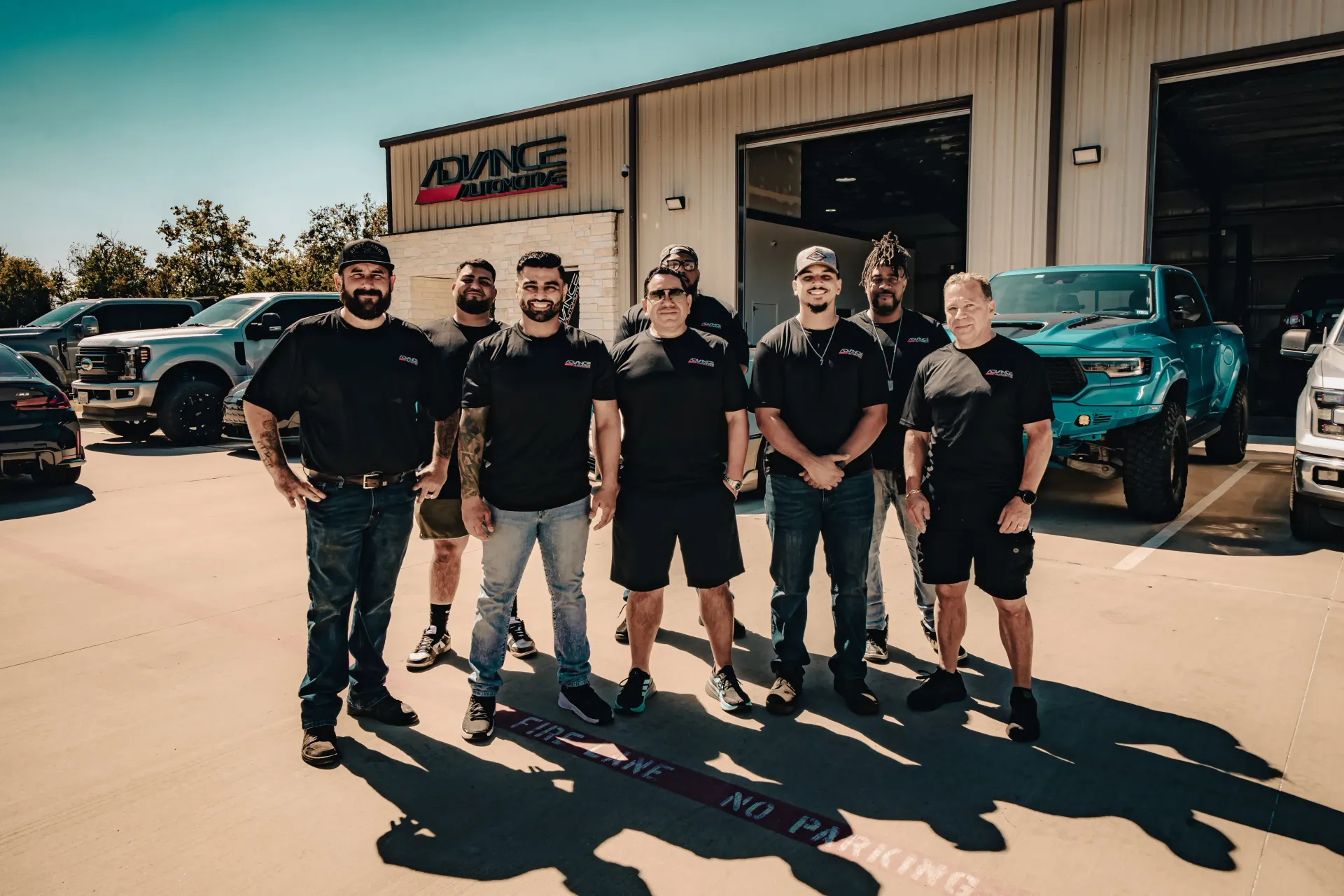 Group of men in black shirts outside a shop with custom trucks. | Advance Automotive
