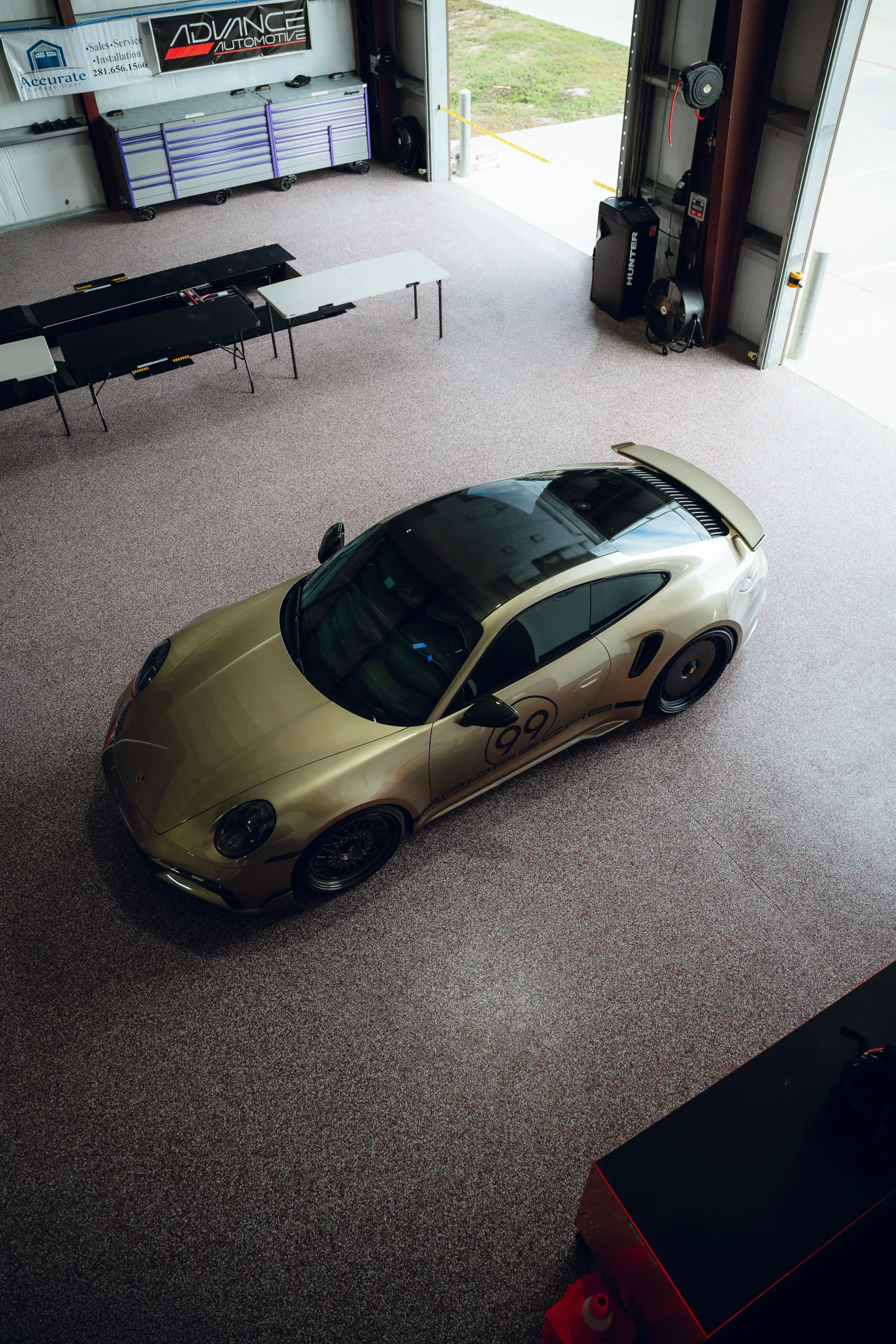 Gold Porsche sports car inside a garage with speckled flooring, black roof, and black wheels. | Advance Automotive