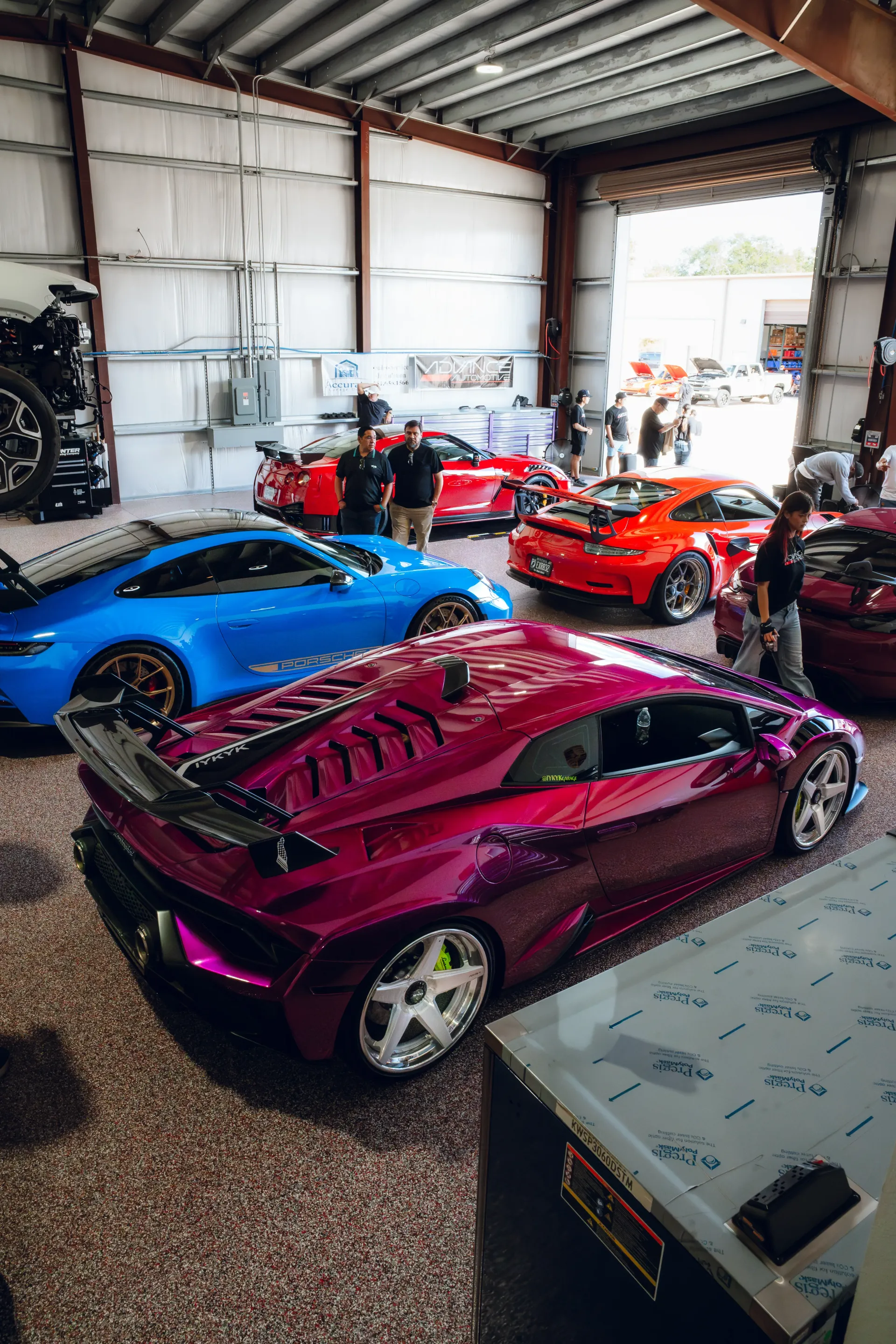 Purple Lamborghini and other colorful sports cars inside a garage with people standing around. | Advance Automotive