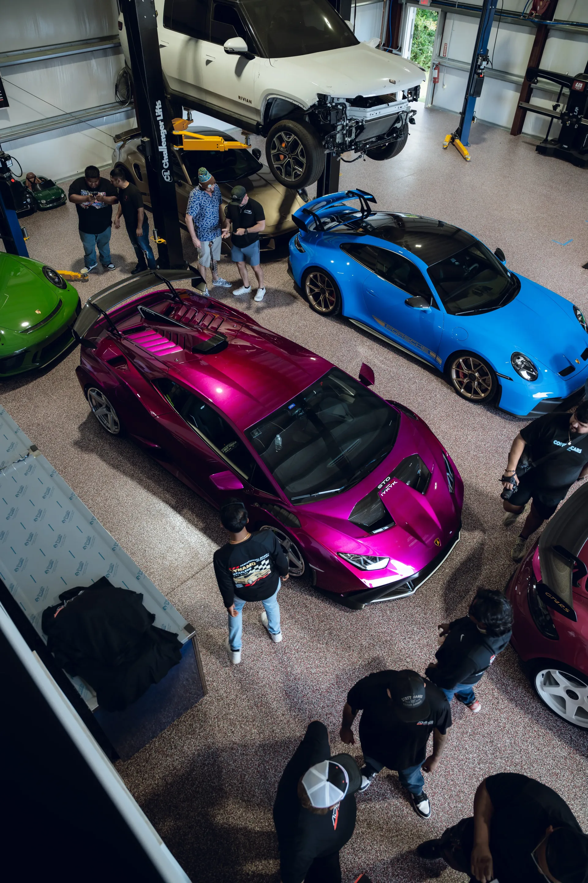 Inside a garage, a purple Lamborghini, blue Porsche, and other cars surrounded by people. | Advance Automotive
