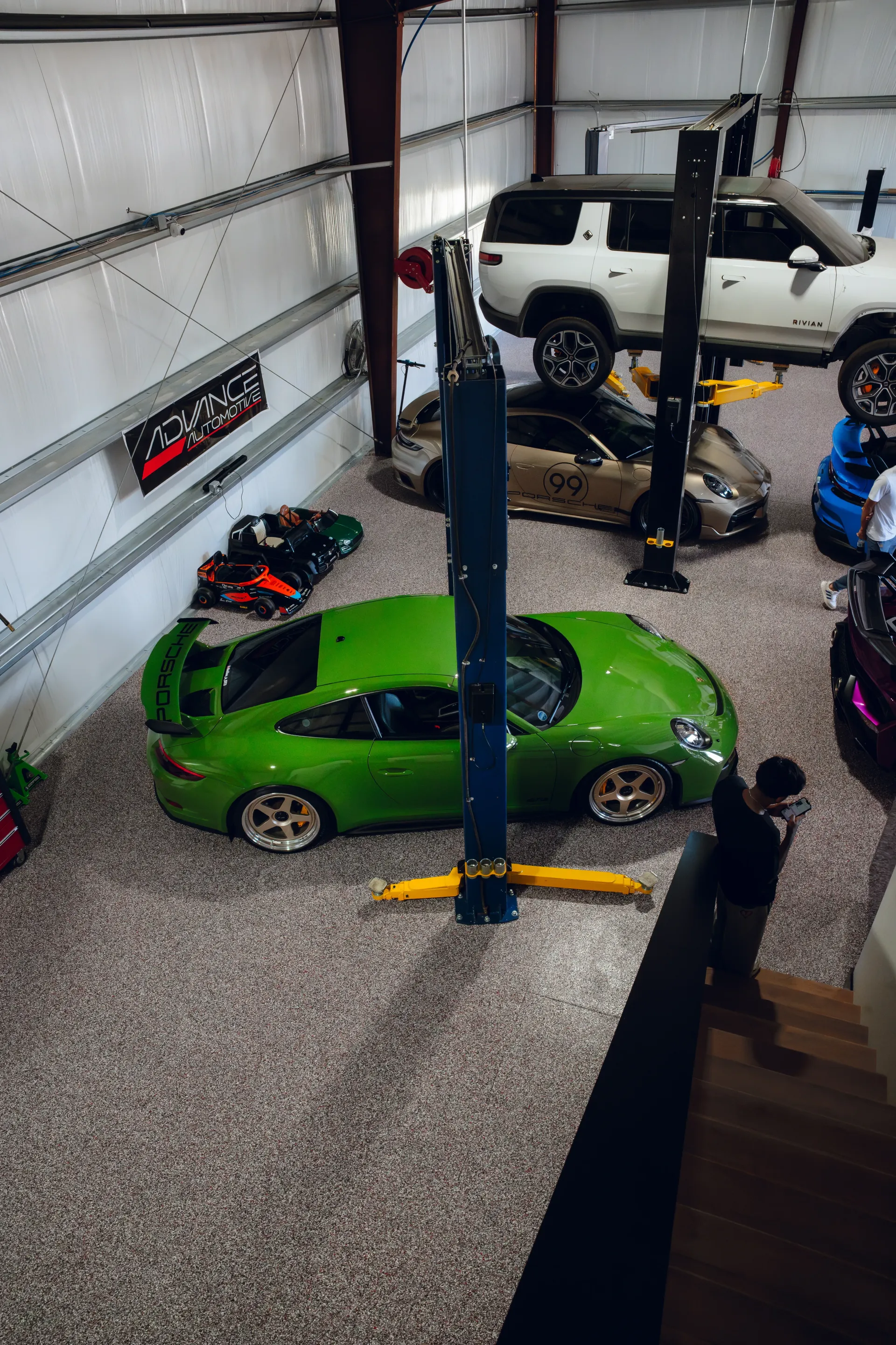 Green sports car in a garage with multiple vehicles, a lift, and a textured floor. | Advance Automotive