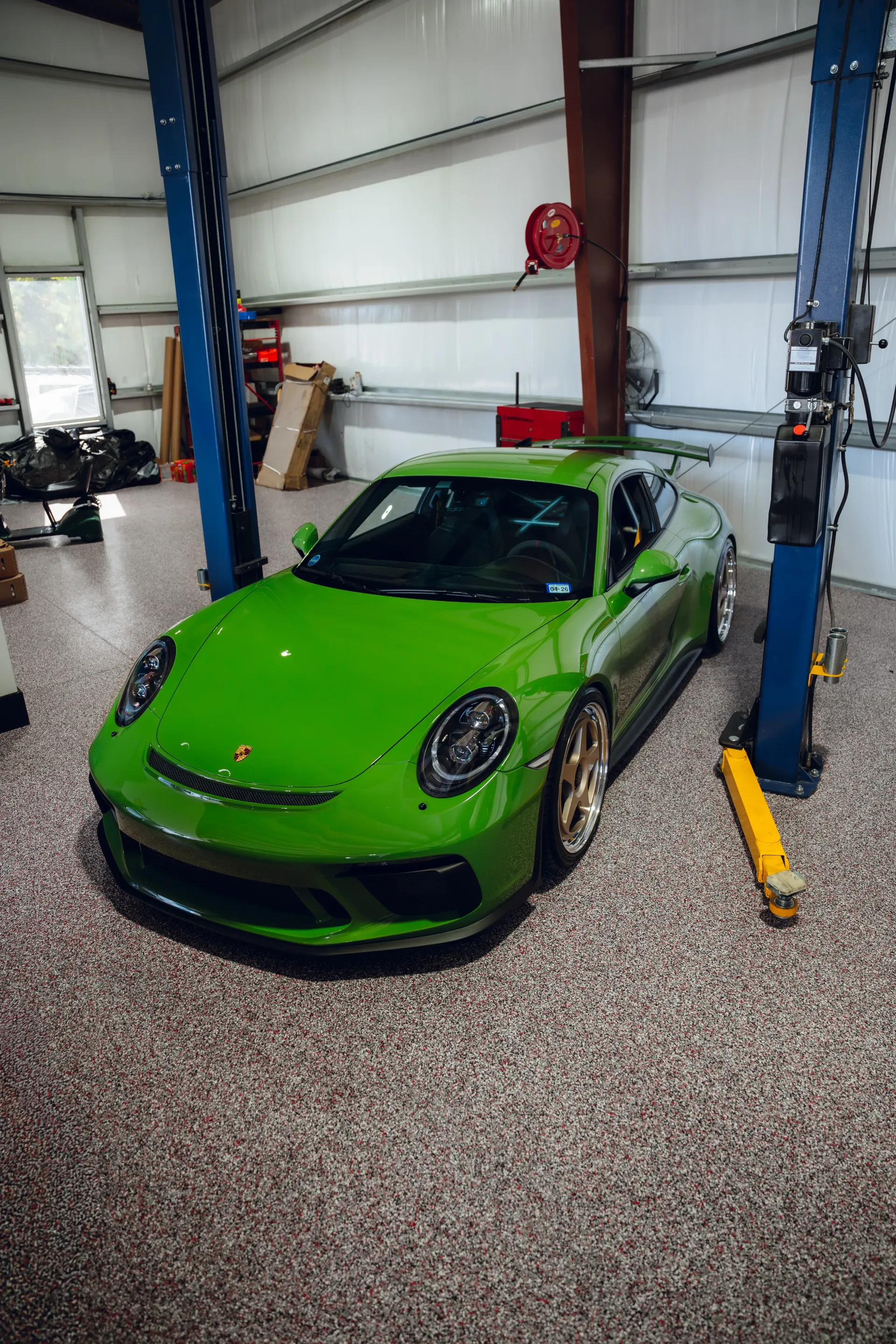 Bright green Porsche 911 in a garage, flanked by blue car lifts, with a speckled floor. | Advance Automotive