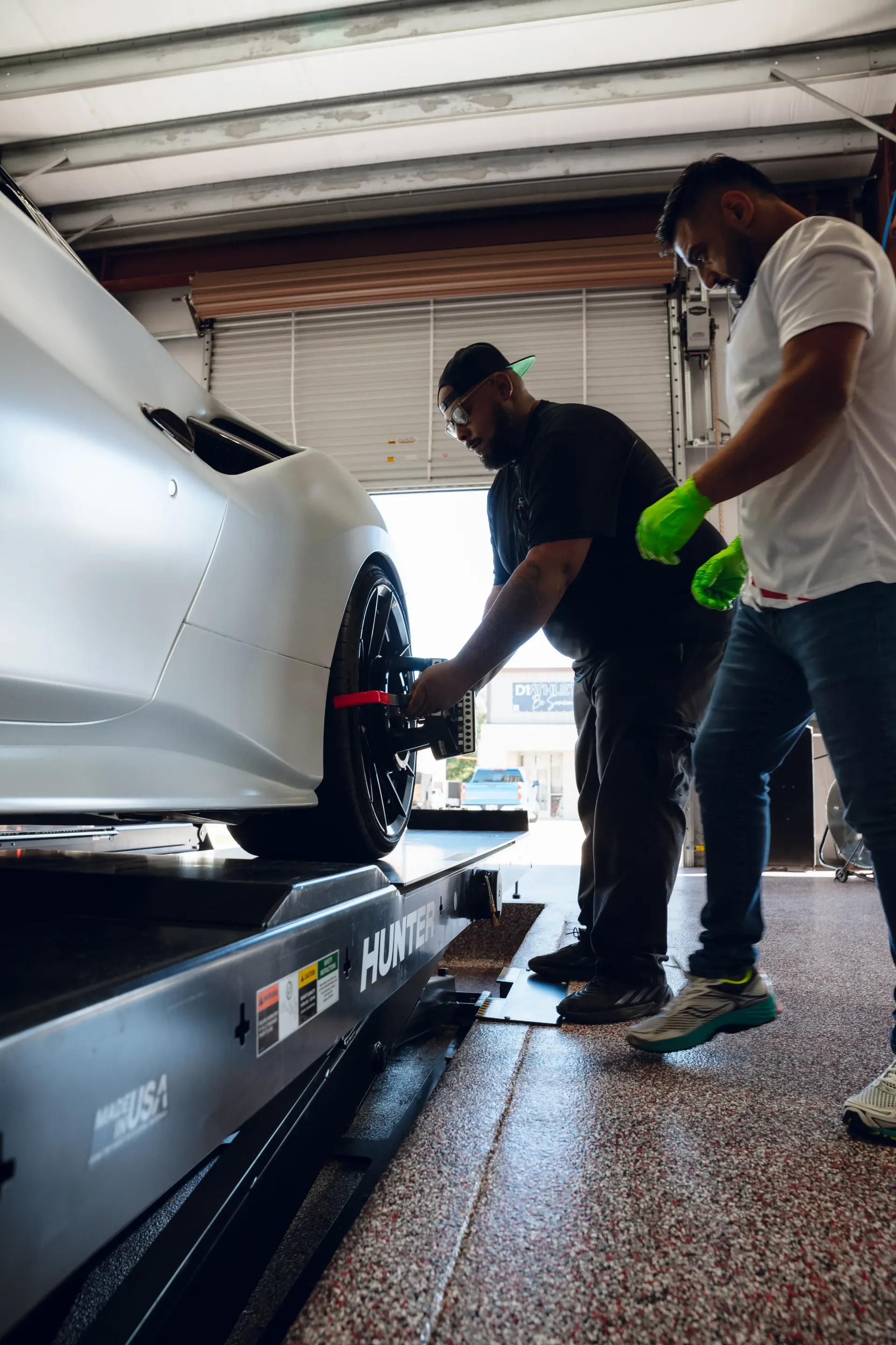 Two men adjusting a car wheel on a lift inside a garage. One wears a black shirt, the other a white one. | Advance Automotive