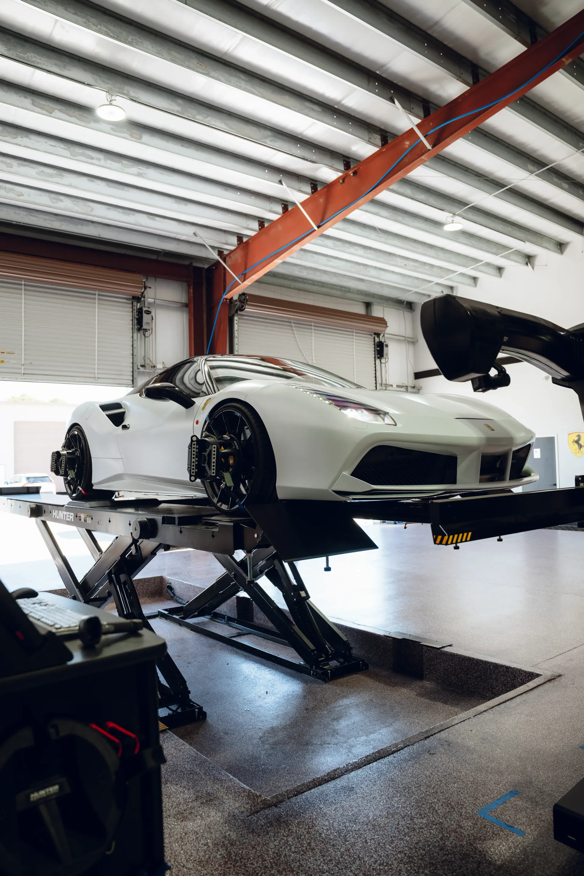 White sports car on a lift in a garage. Black wheels, red beams, and a gray floor. | Advance Automotive
