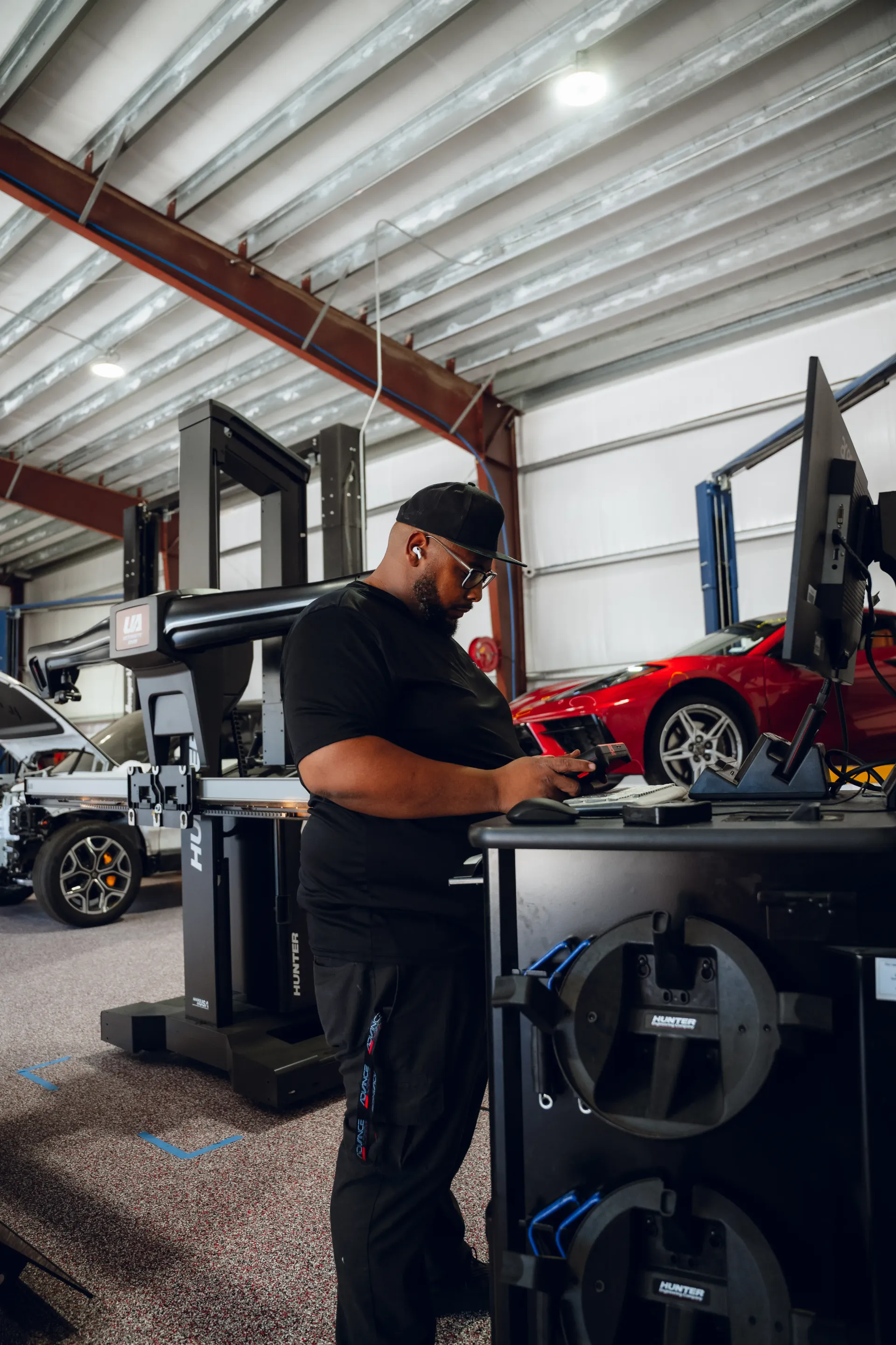 Mechanic working on car alignment equipment in a garage. Red car in background. | Advance Automotive