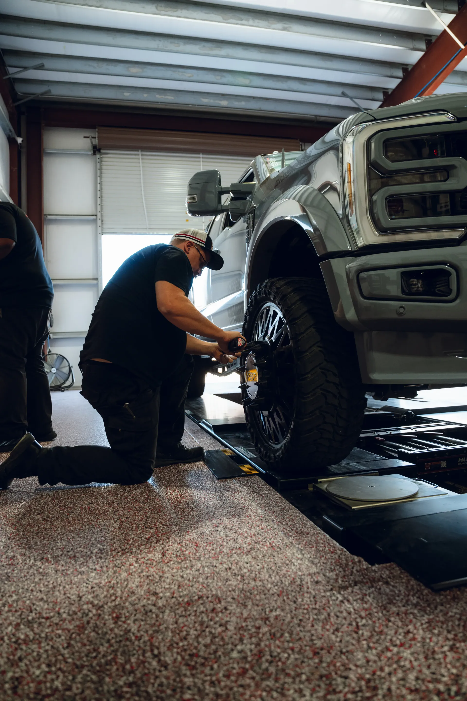 Man kneeling, working on the front wheel of a gray pickup truck inside a garage. | Advance Automotive