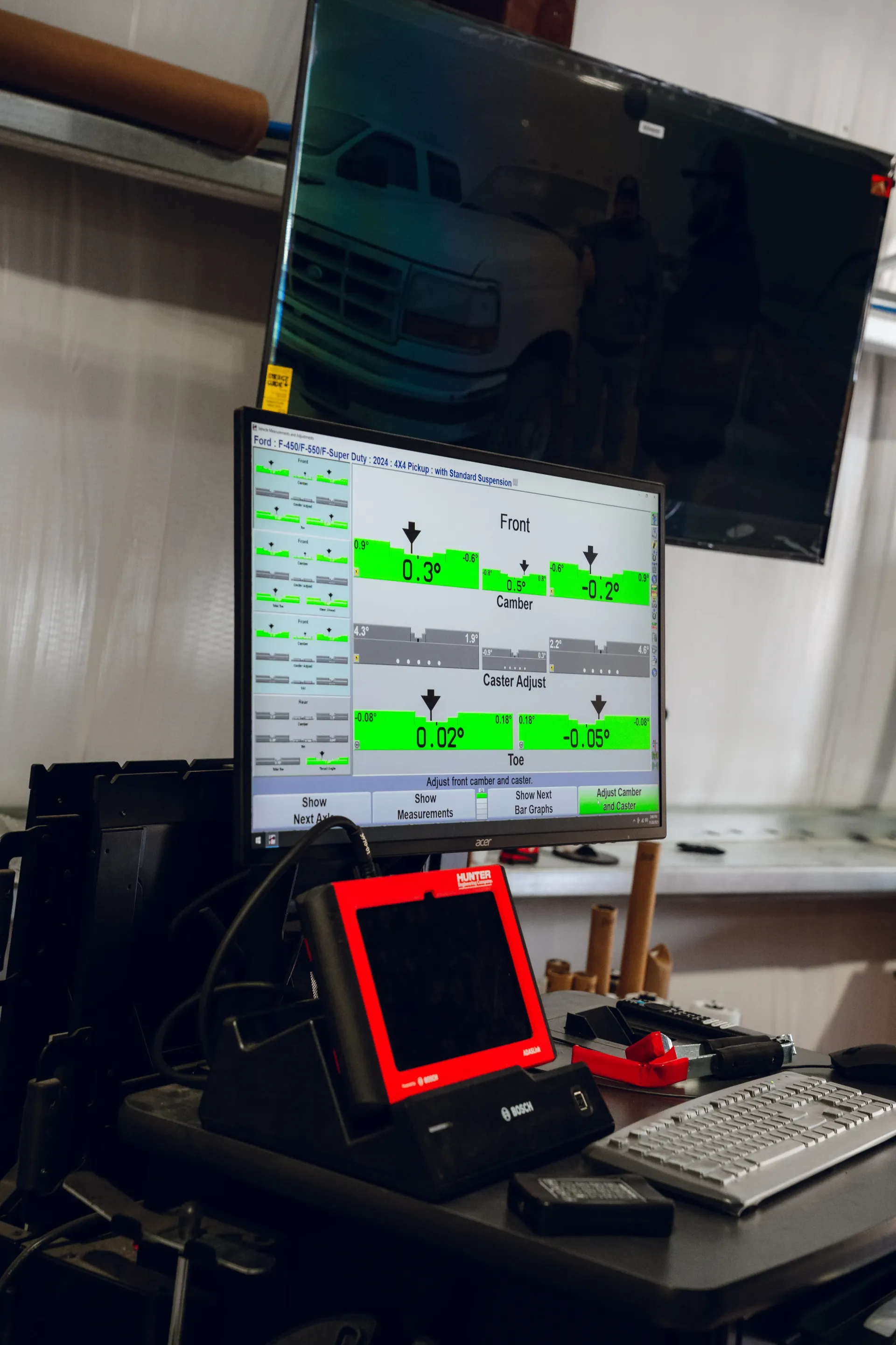 Alignment machine with monitors displaying vehicle data, red diagnostic tool, keyboard, and van reflection. | Advance Automotive