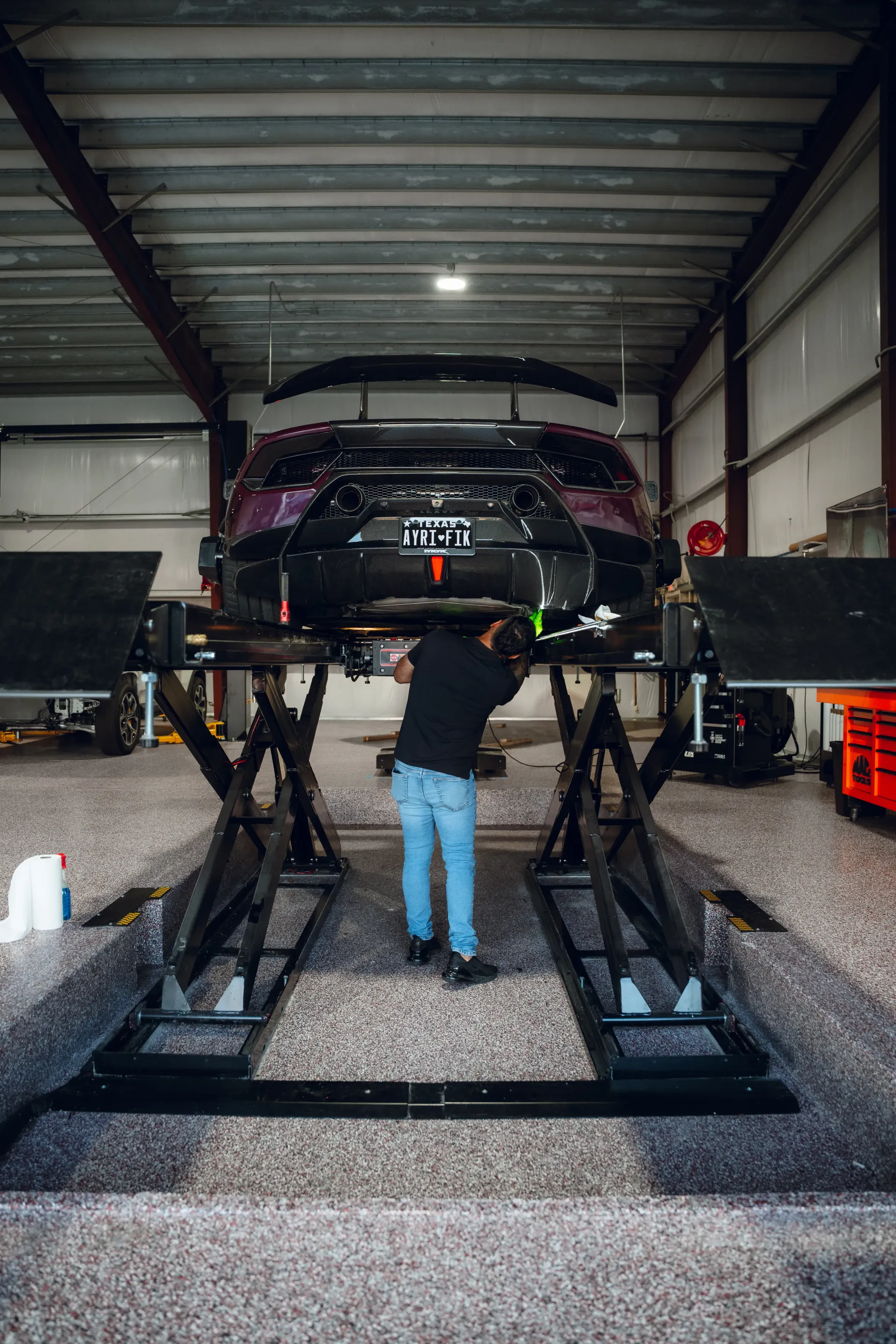Mechanic working under a black sports car raised on a lift in a garage. | Advance Automotive