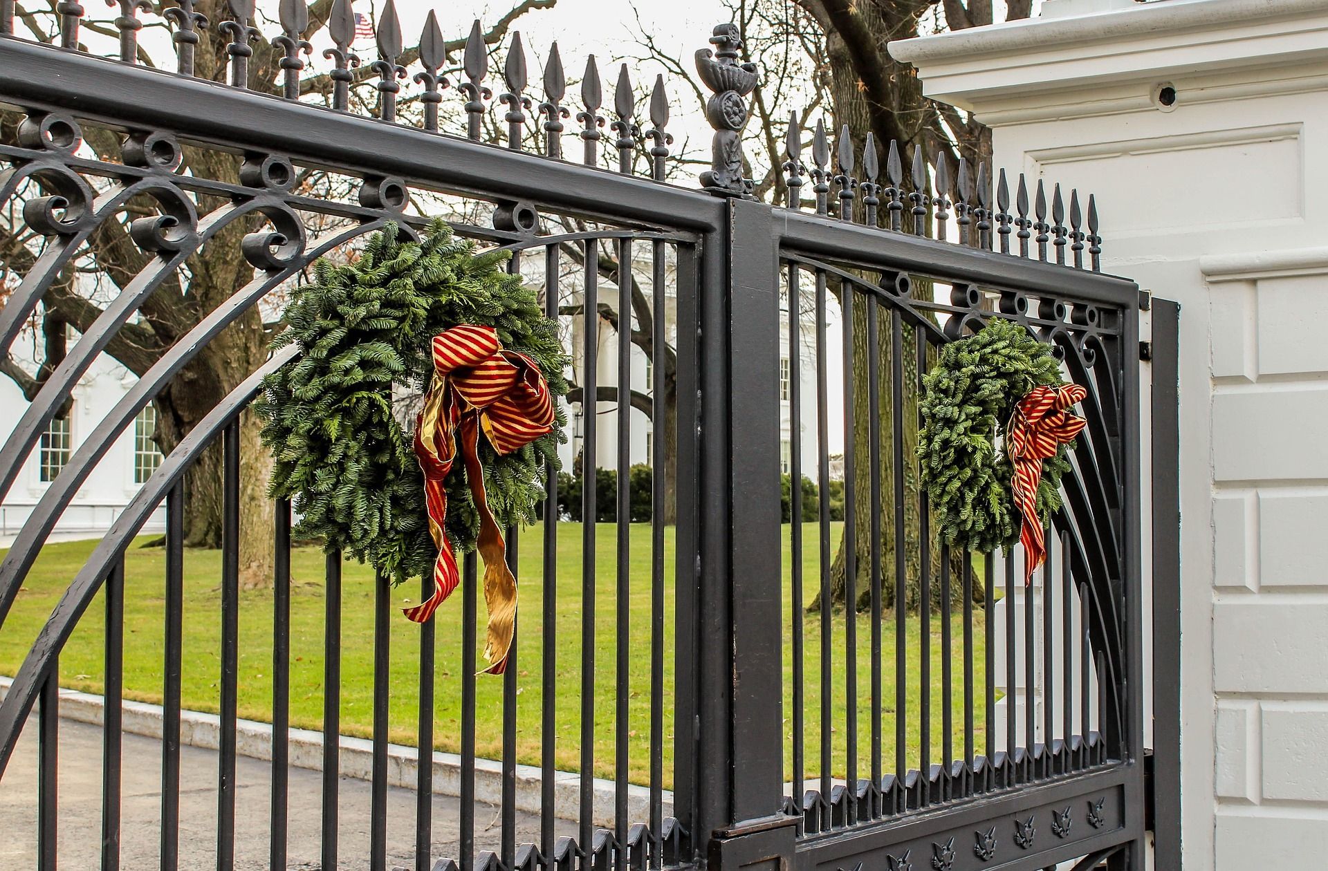 Black wrought-iron gate decorated with orange-and-black bows beside a white building and green lawn