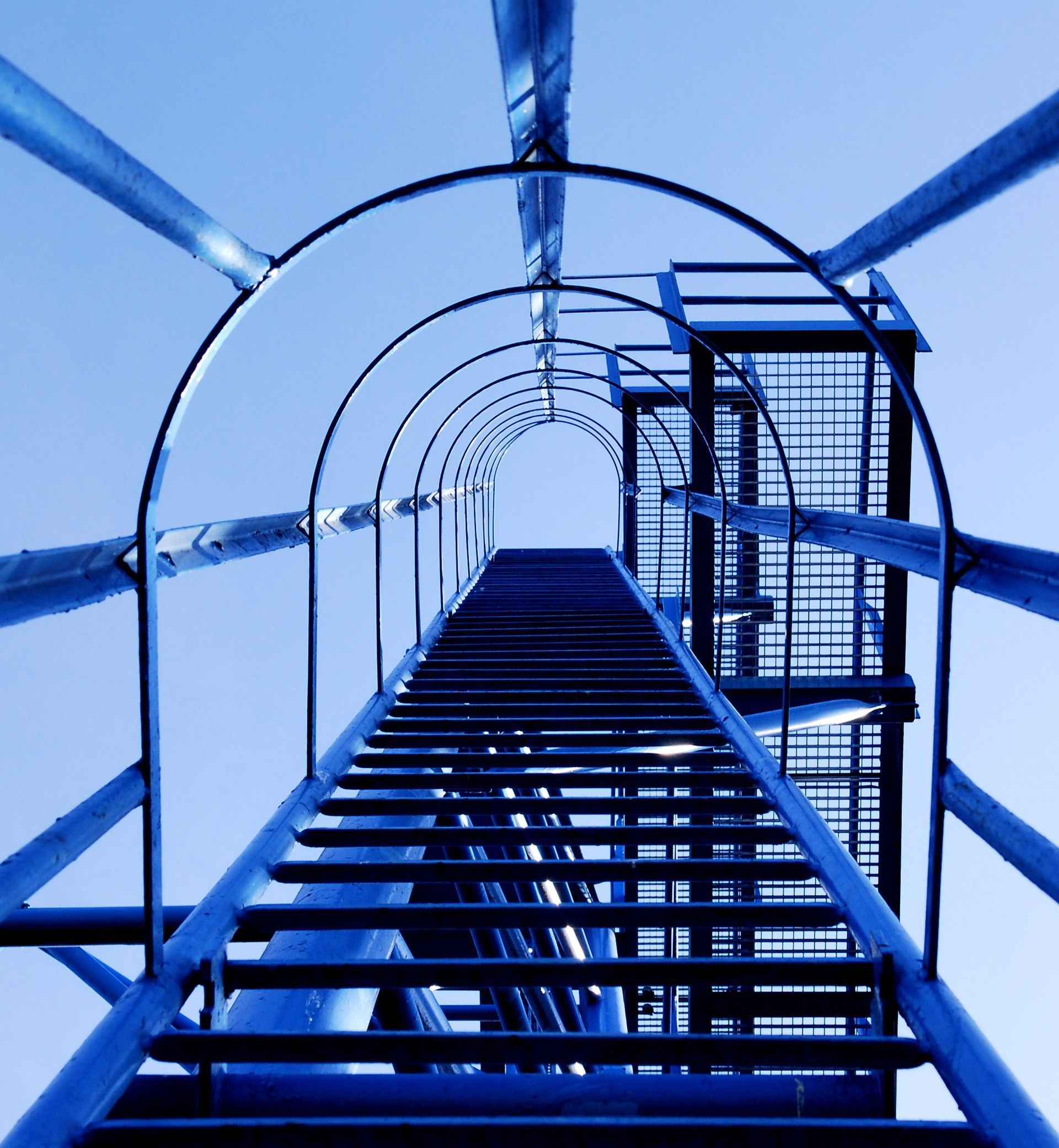 Blue metal fire escape ladder viewed upward against a bright sky