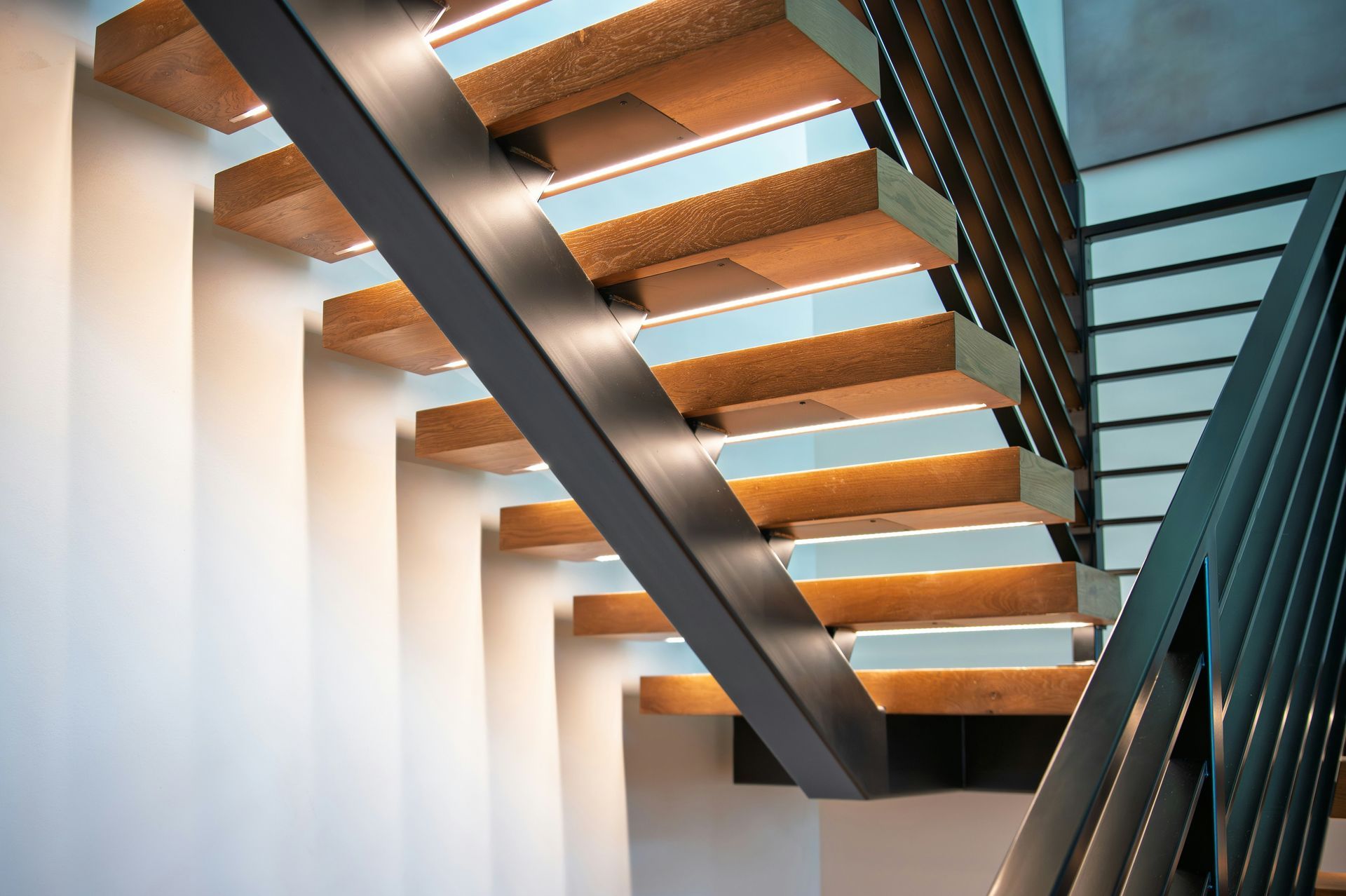 Modern staircase with wooden treads, dark railings, and white walls in a bright interior