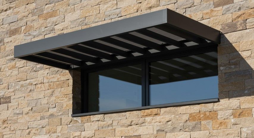 Window with dark metal awning, set in a stone wall.