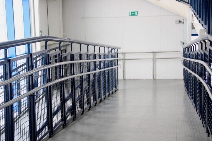 Ramp with metal railings, leading down a hallway with white walls and emergency exit sign.