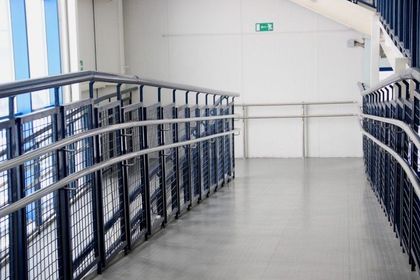 Ramp with metal railings, leading down a hallway with white walls and emergency exit sign.