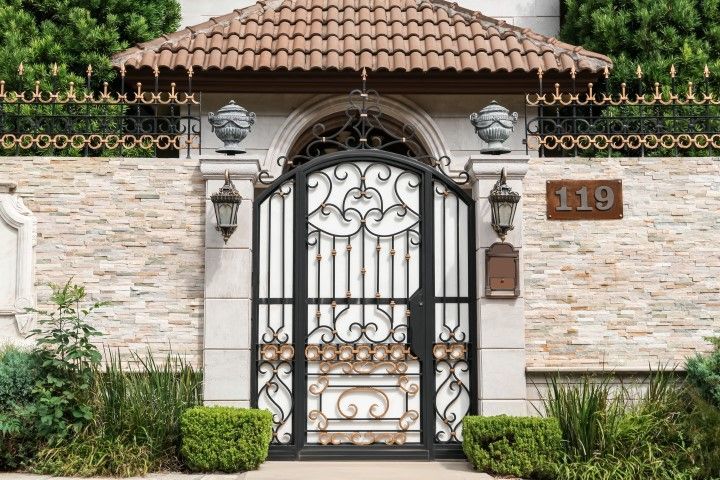 An ornate iron gate at the entrance of a building with stone walls.
