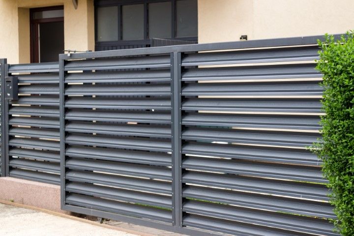 Gray horizontal slat fence in front of a building and some bushes