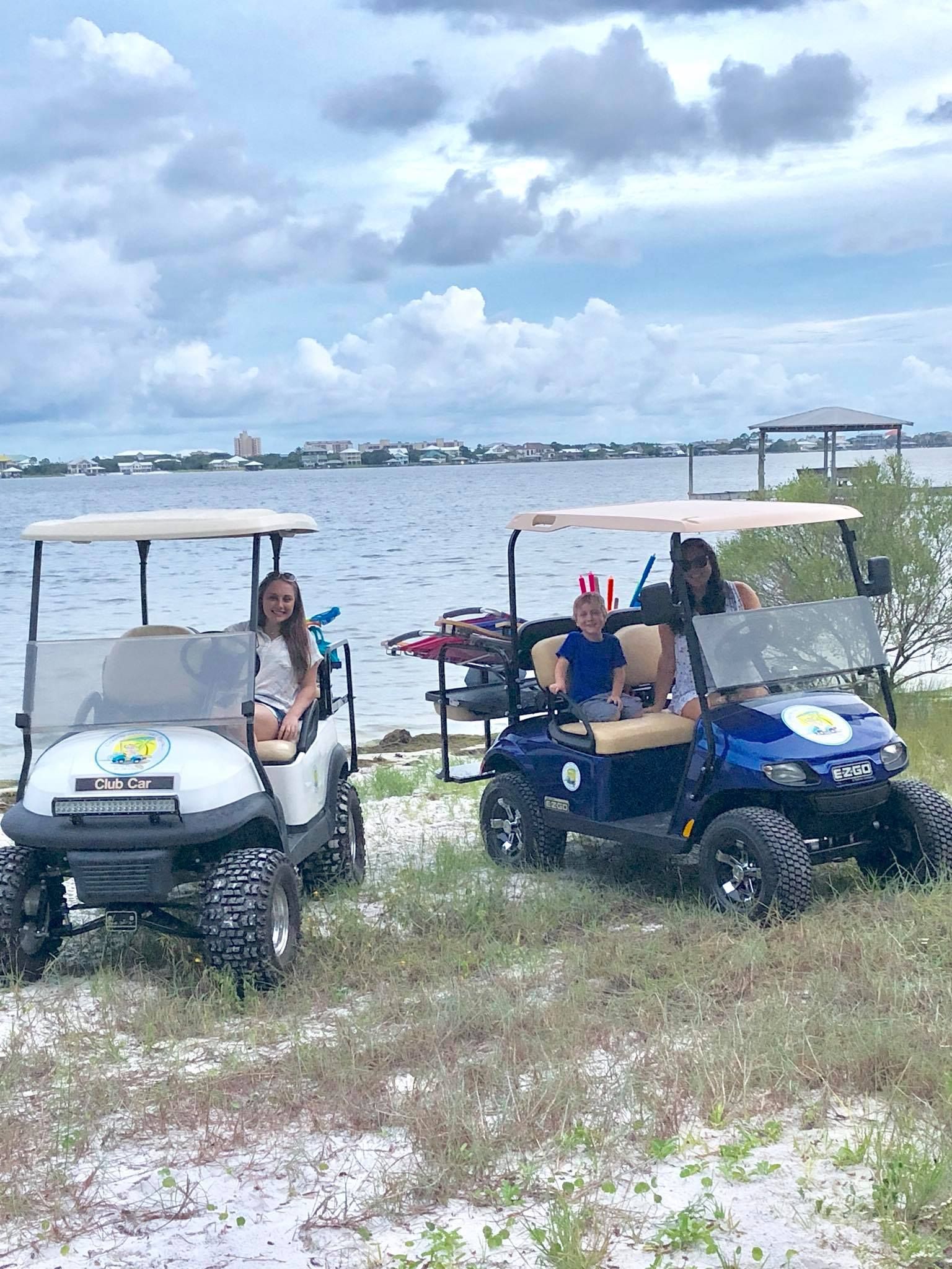 Two people in separate golf carts parked on a sandy beach shore by a body of water under a cloudy sky.