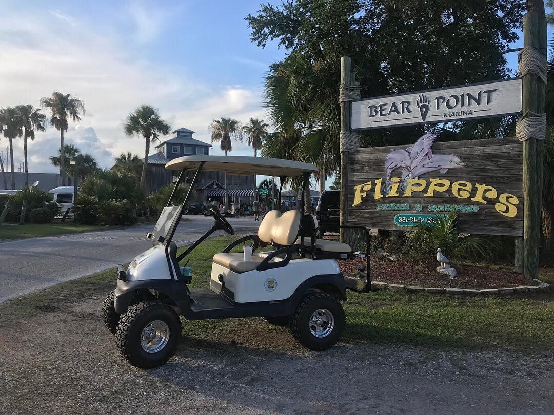 A white golf cart parked next to a wooden sign for 