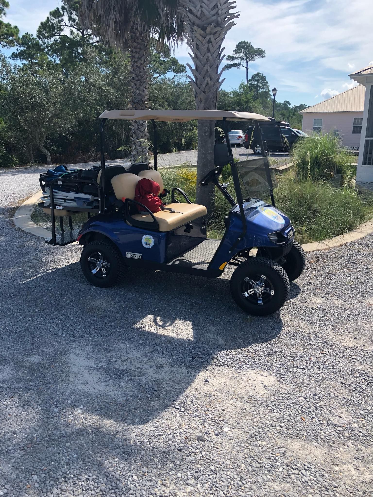 A dark blue golf cart parked on a gravel driveway in front of palm trees and a house on a sunny day.