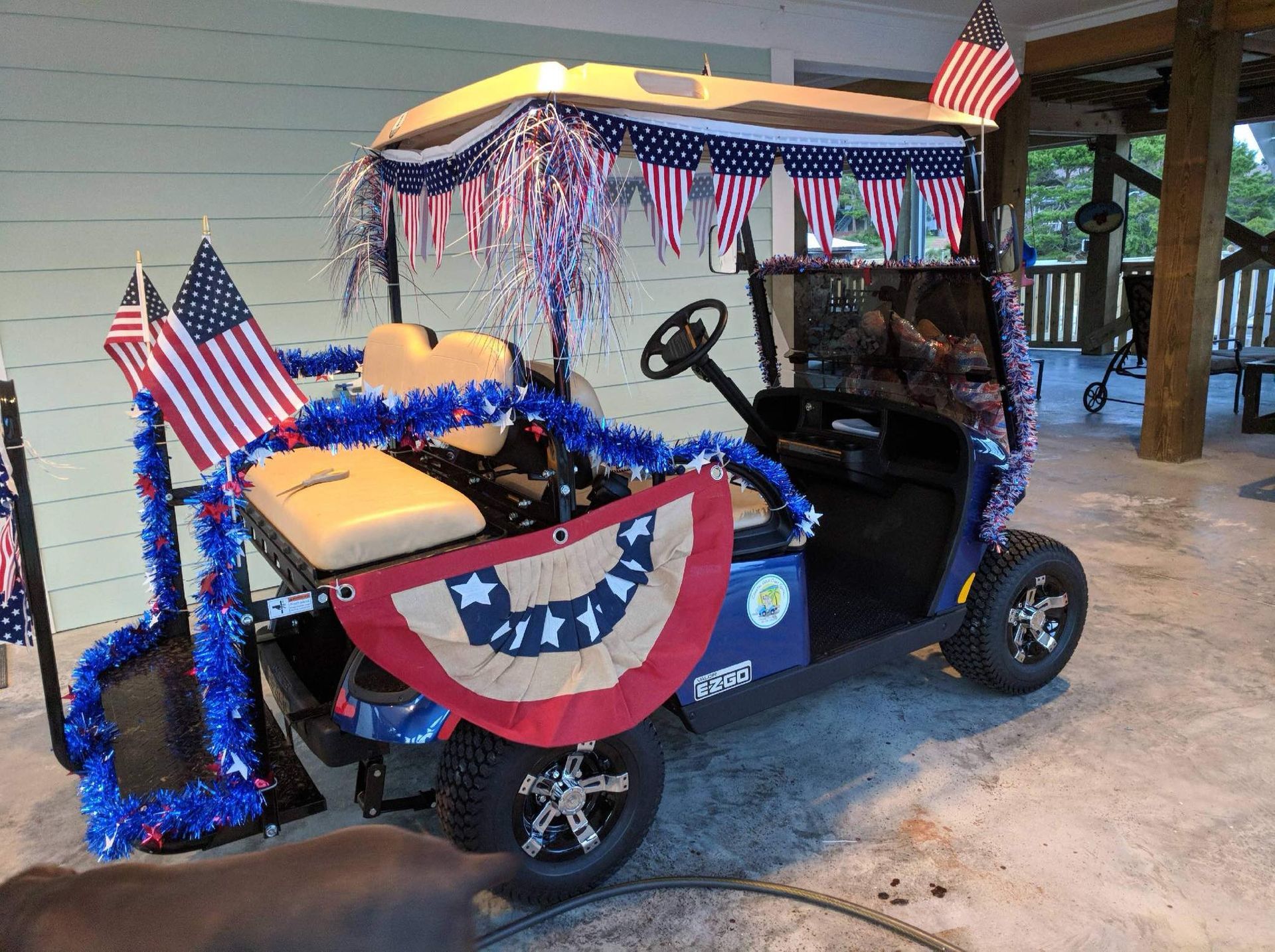 A golf cart decorated with American flags, red-white-and-blue tinsel, and bunting, parked on a porch.