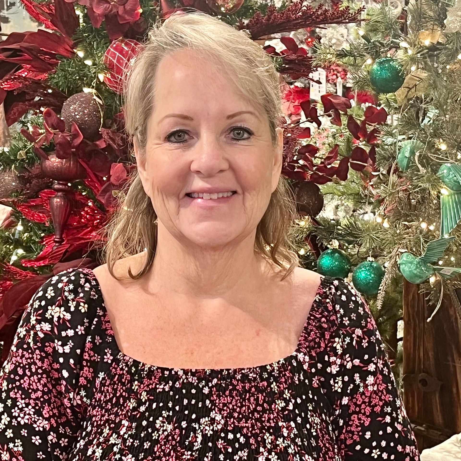 A woman is smiling in front of a christmas tree.