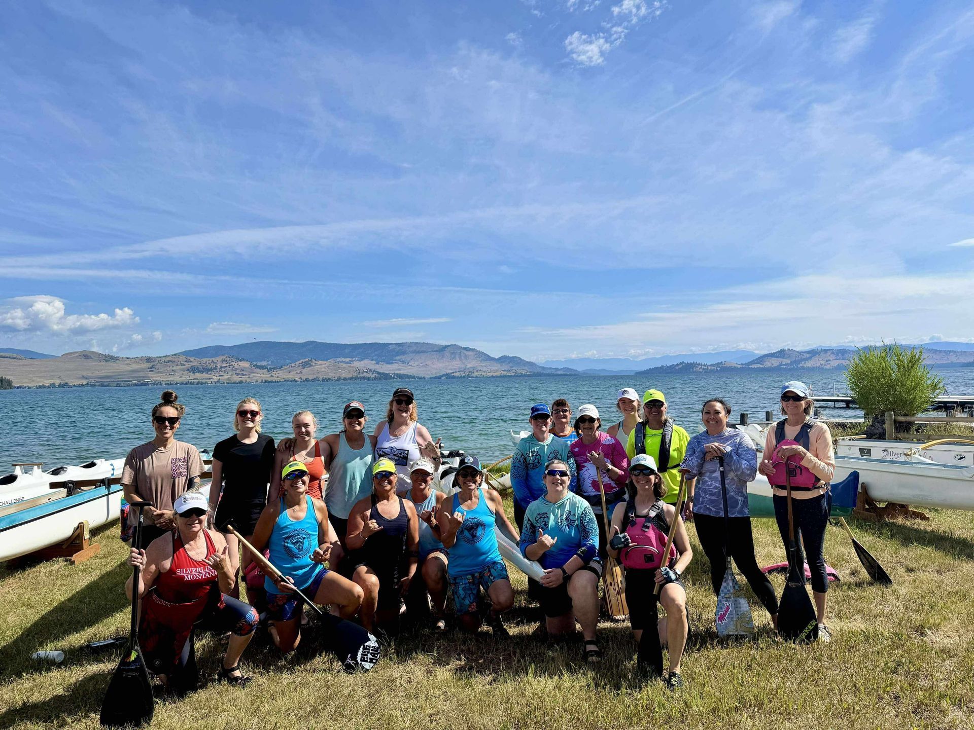 Group of people posing by a lake. Sunny day, blue sky, mountains in the distance.