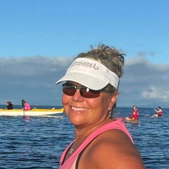 A woman wearing a pink tank top and a white hat stands in the water