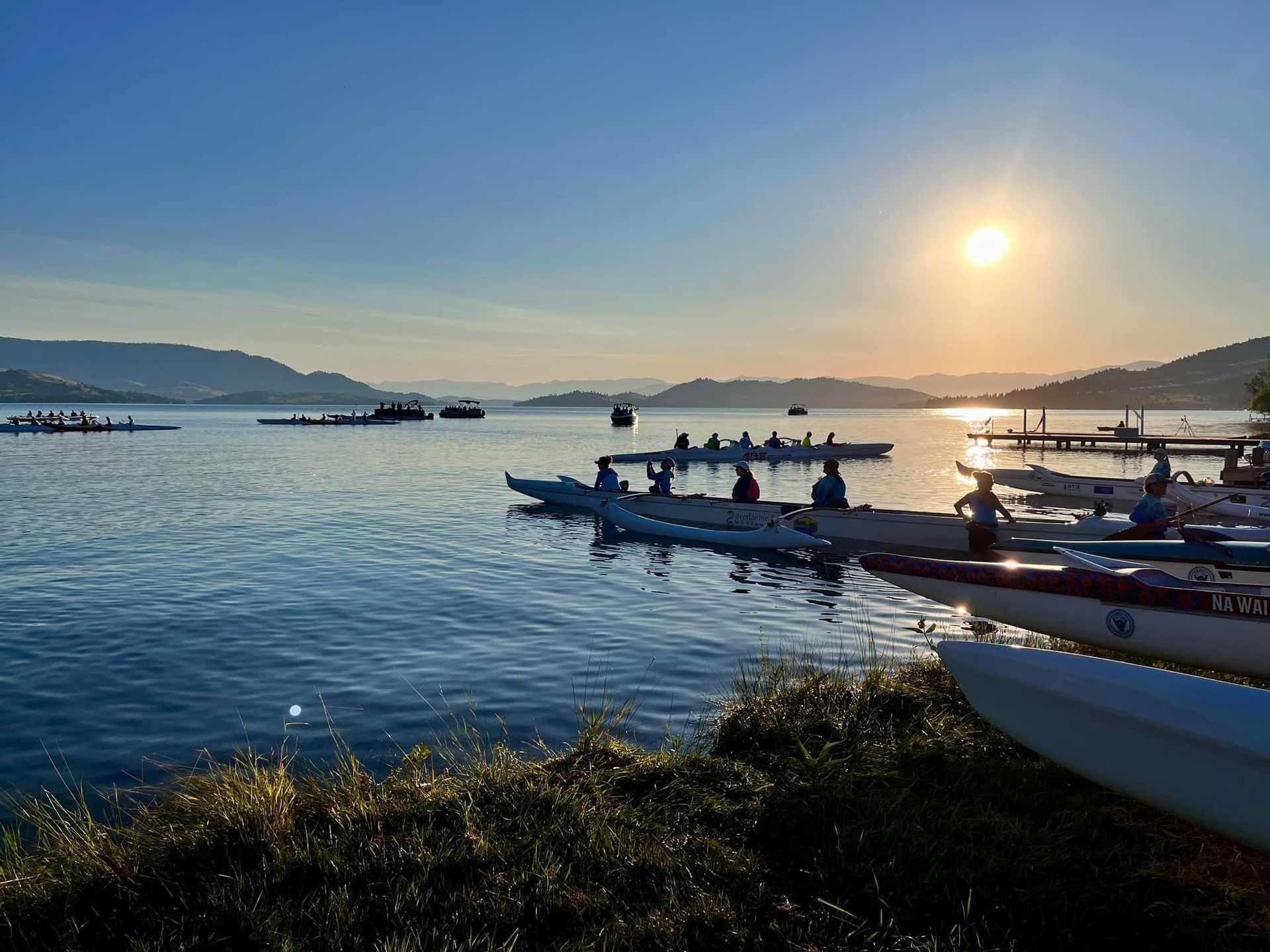 A group of people are in kayaks on a lake at sunset.
