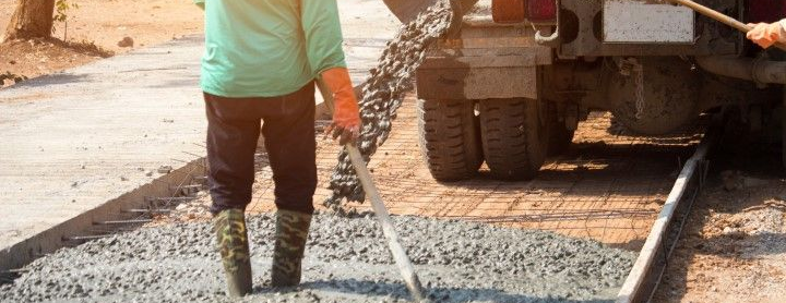 A truck is pouring out concrete cement on the road while being spread out by the worker.