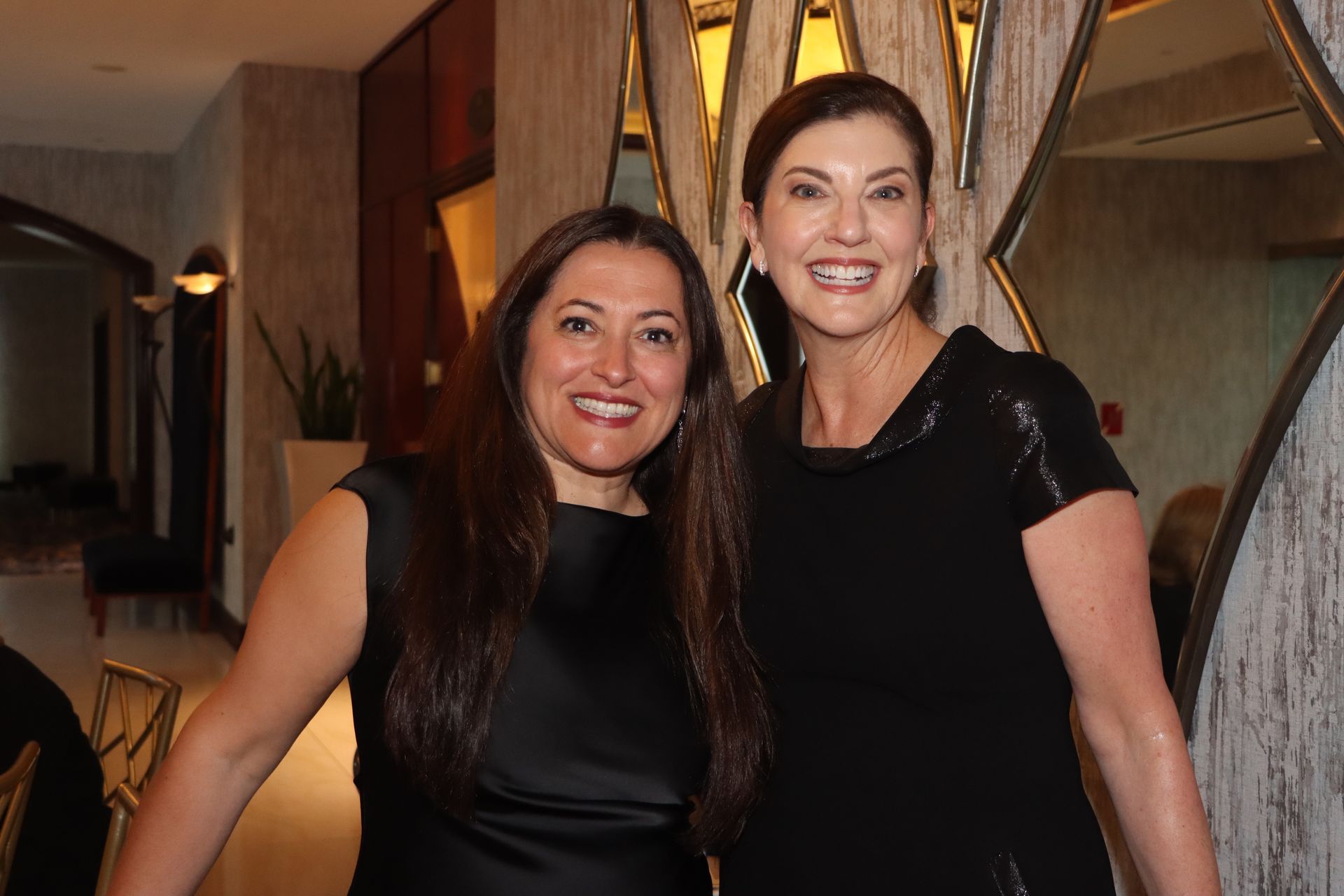 Two women in black dresses are posing for a picture together.