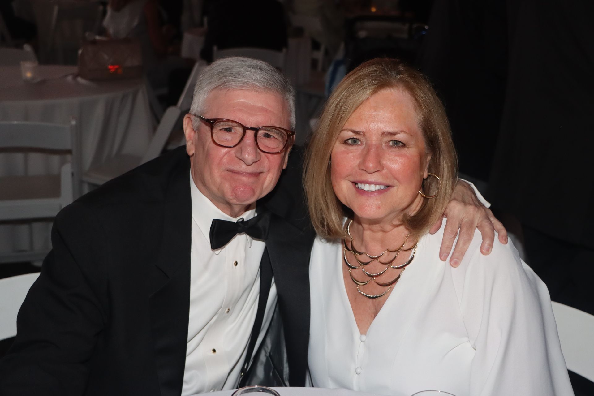 A man in a tuxedo and a woman in a white shirt are posing for a picture.