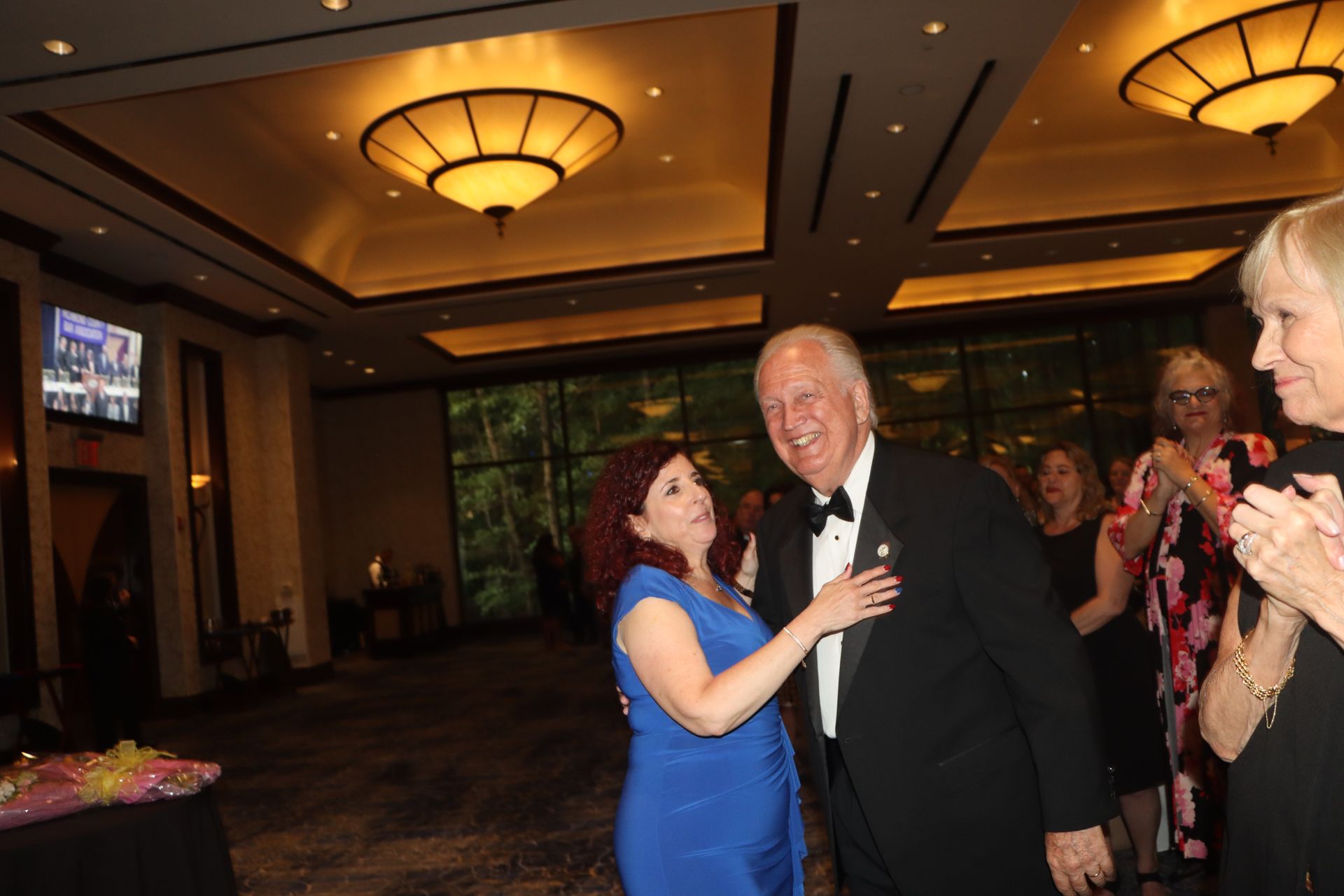 A woman in a blue dress is hugging a man in a tuxedo