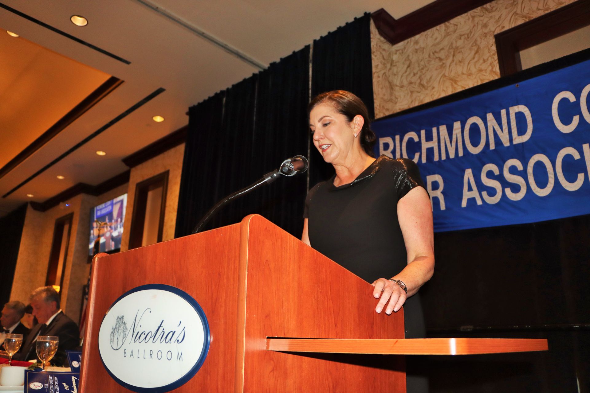 A woman stands at a podium in front of a sign that says richmond county bar association